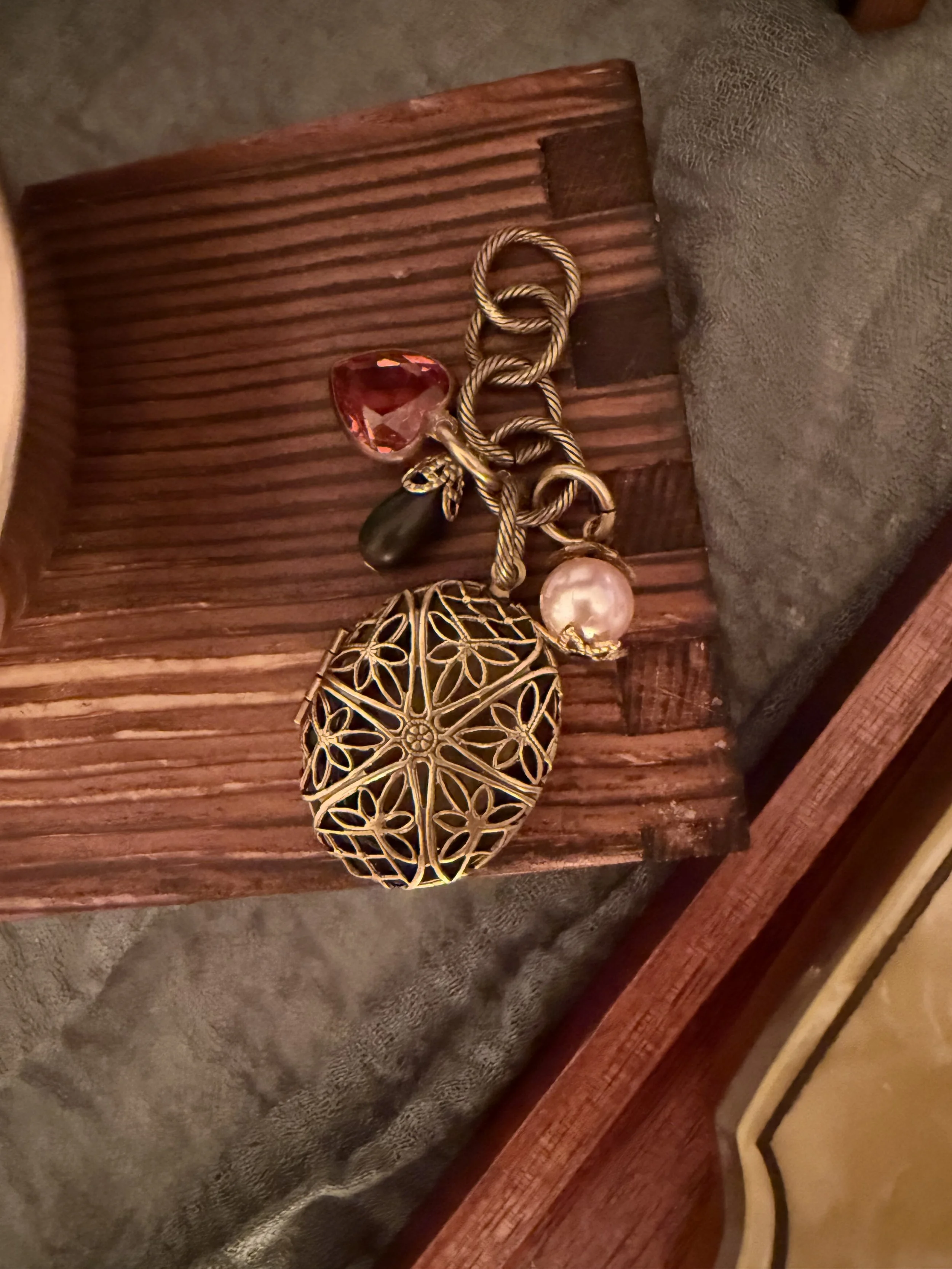 Decorative object with gold lattice design, a pearl, an ornate gold and black cone-shaped item, a gold and black twisted rope, a red gemstone, and a black teardrop-shaped ornament, all on a wooden surface.