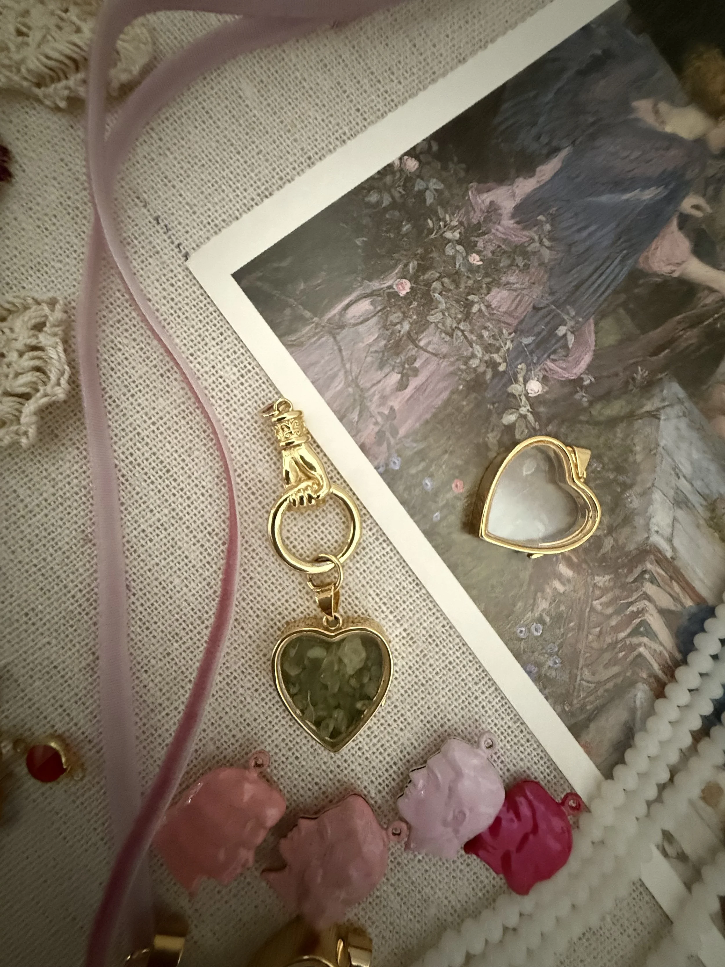 A photo of various jewelry pieces, including heart-shaped pendants with dark stones, gold-colored rings, and other decorative items, displayed on a textured surface.