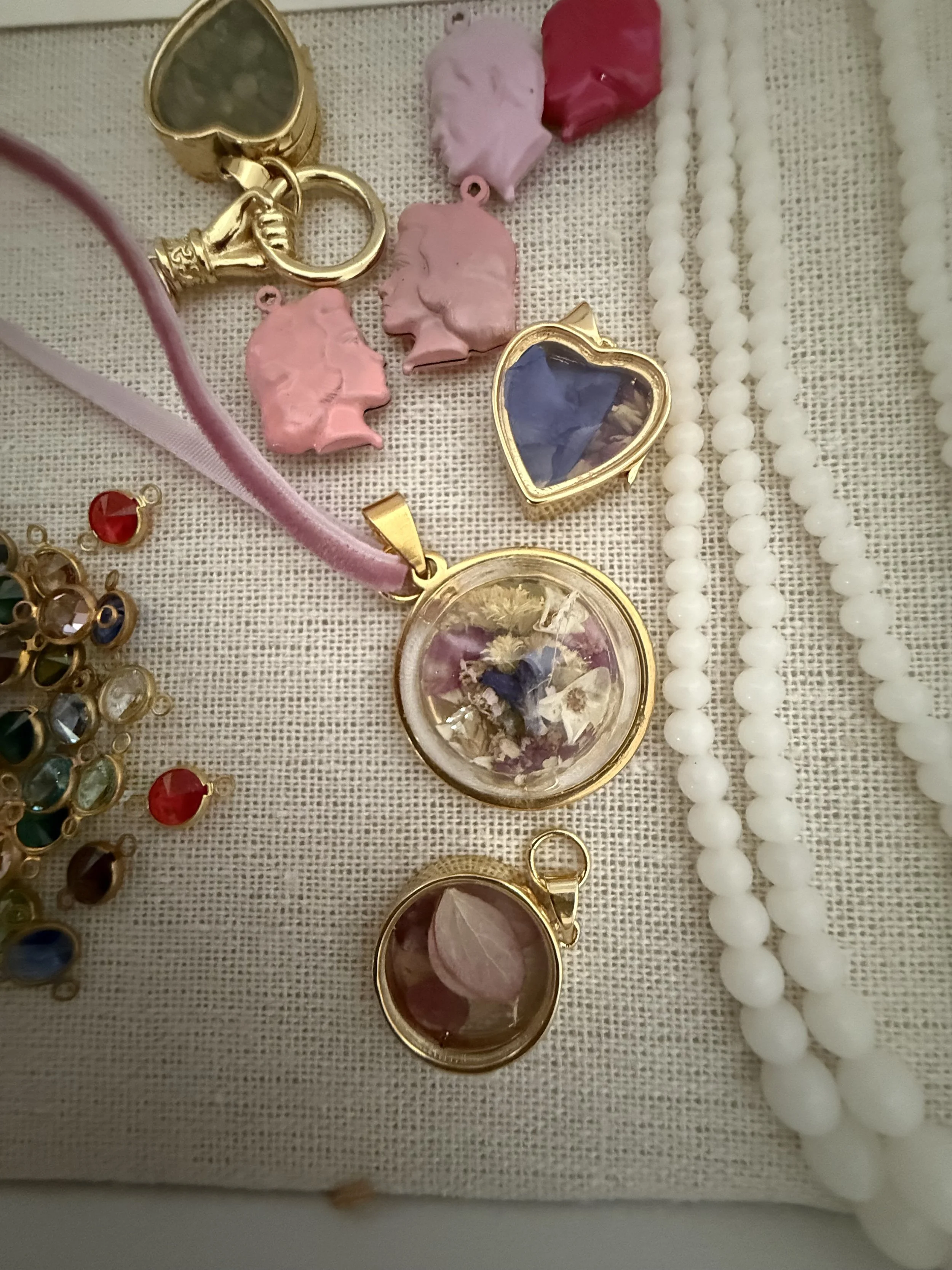 Assorted jewelry including heart-shaped charms, cameo pendants, and pearl necklaces displayed on a fabric surface.