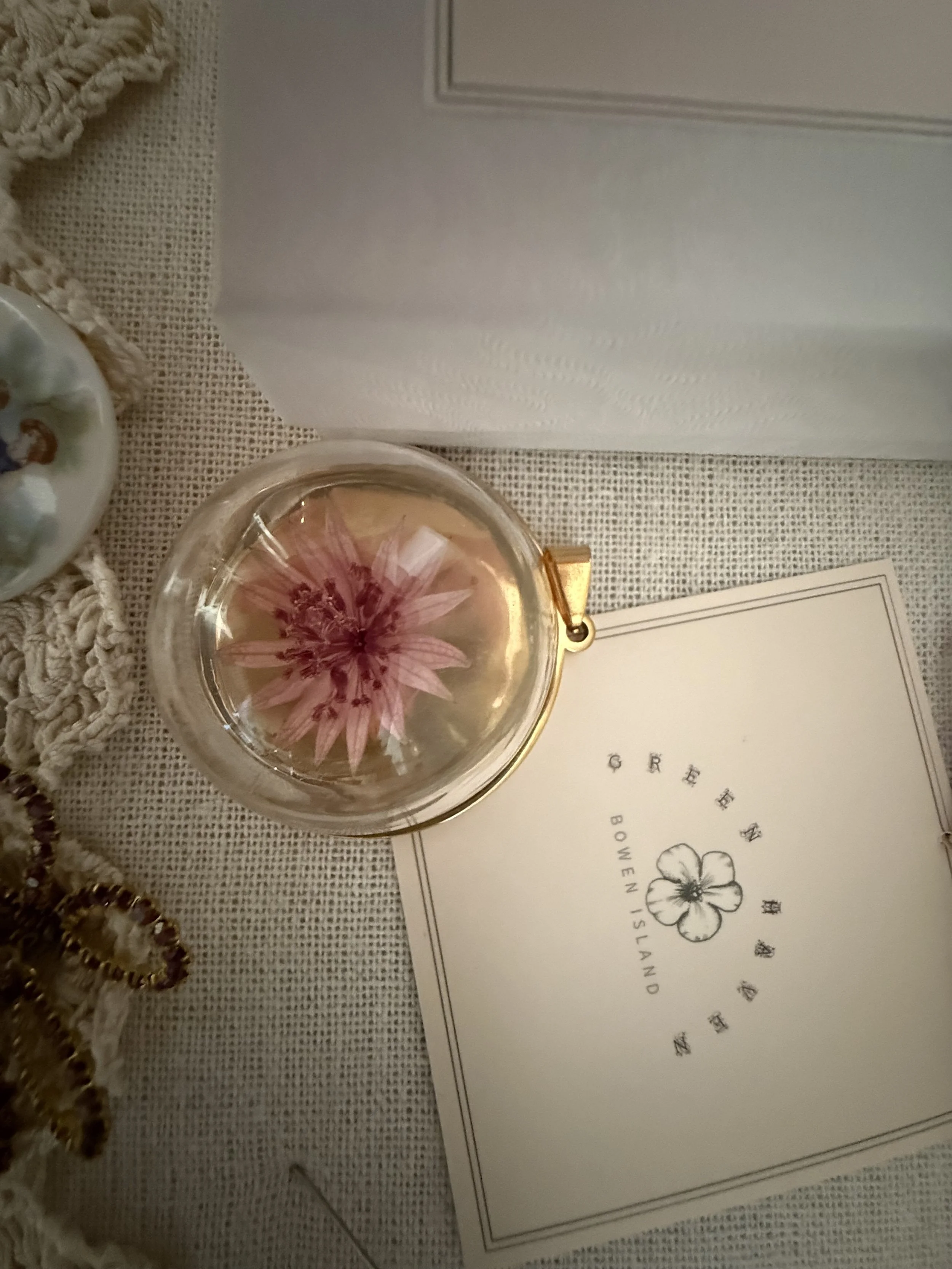 A glass with a flower inside, placed on a textured fabric surface next to a piece of paper with a flower illustration and text.