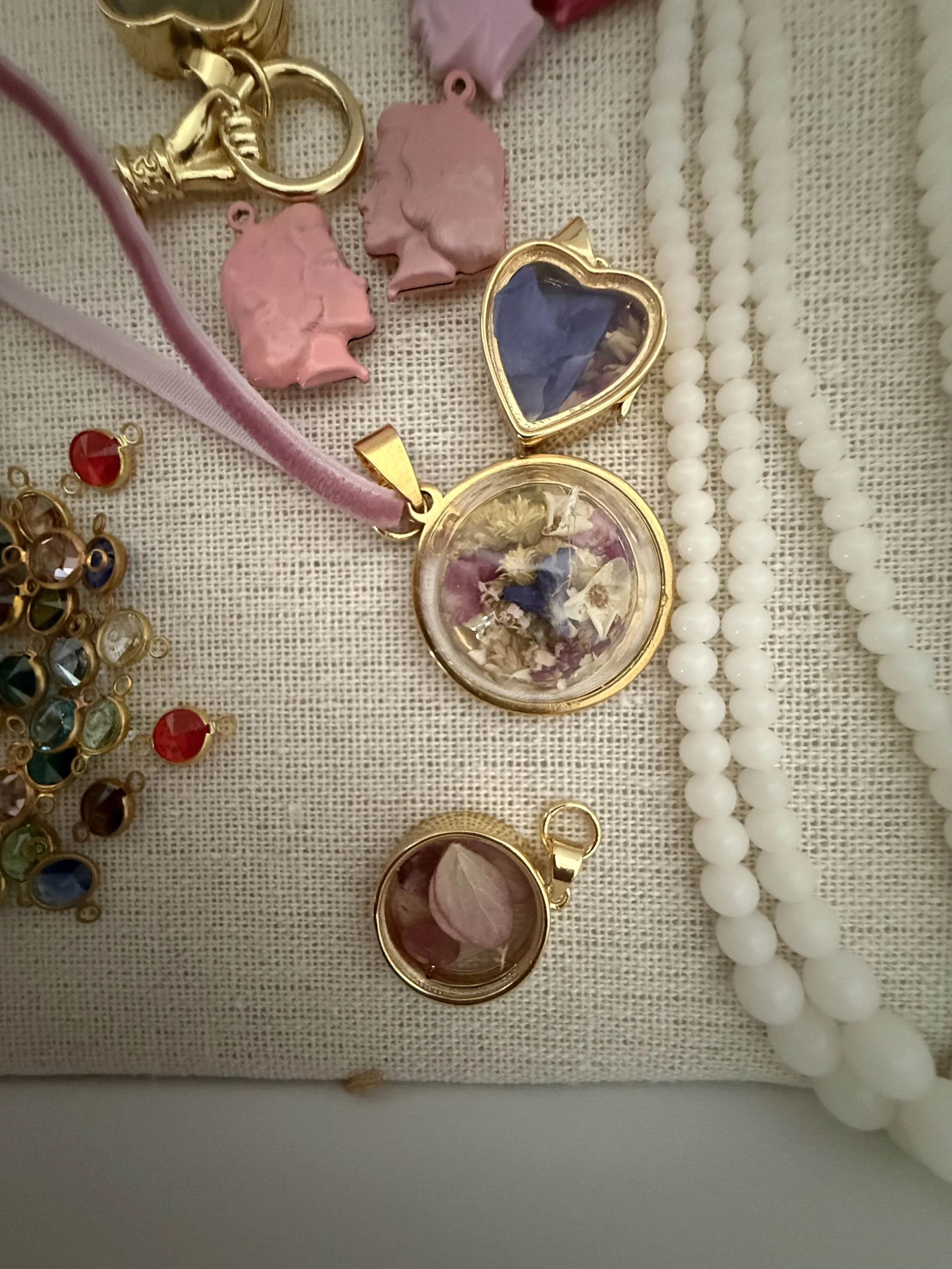 Collection of jewelry including gold chains, pendants, and a string of white beads displayed on a beige fabric background.
