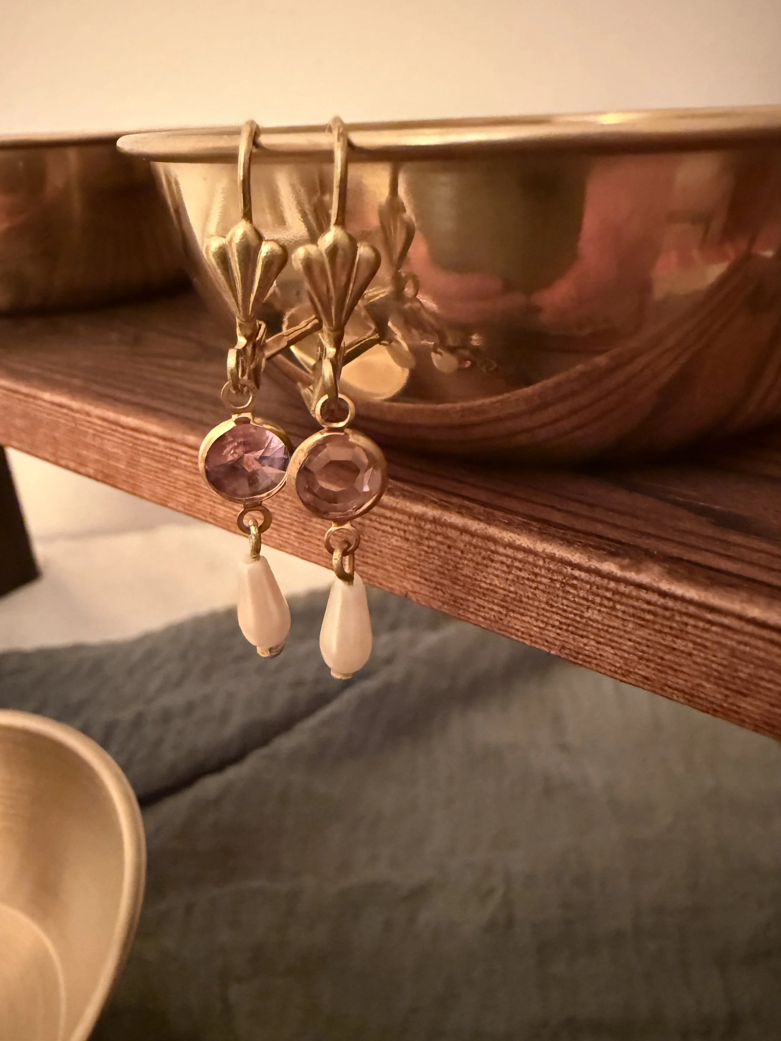 Gold earrings with pink and white teardrop-shaped stones hanging from a mirror or jewelry display.