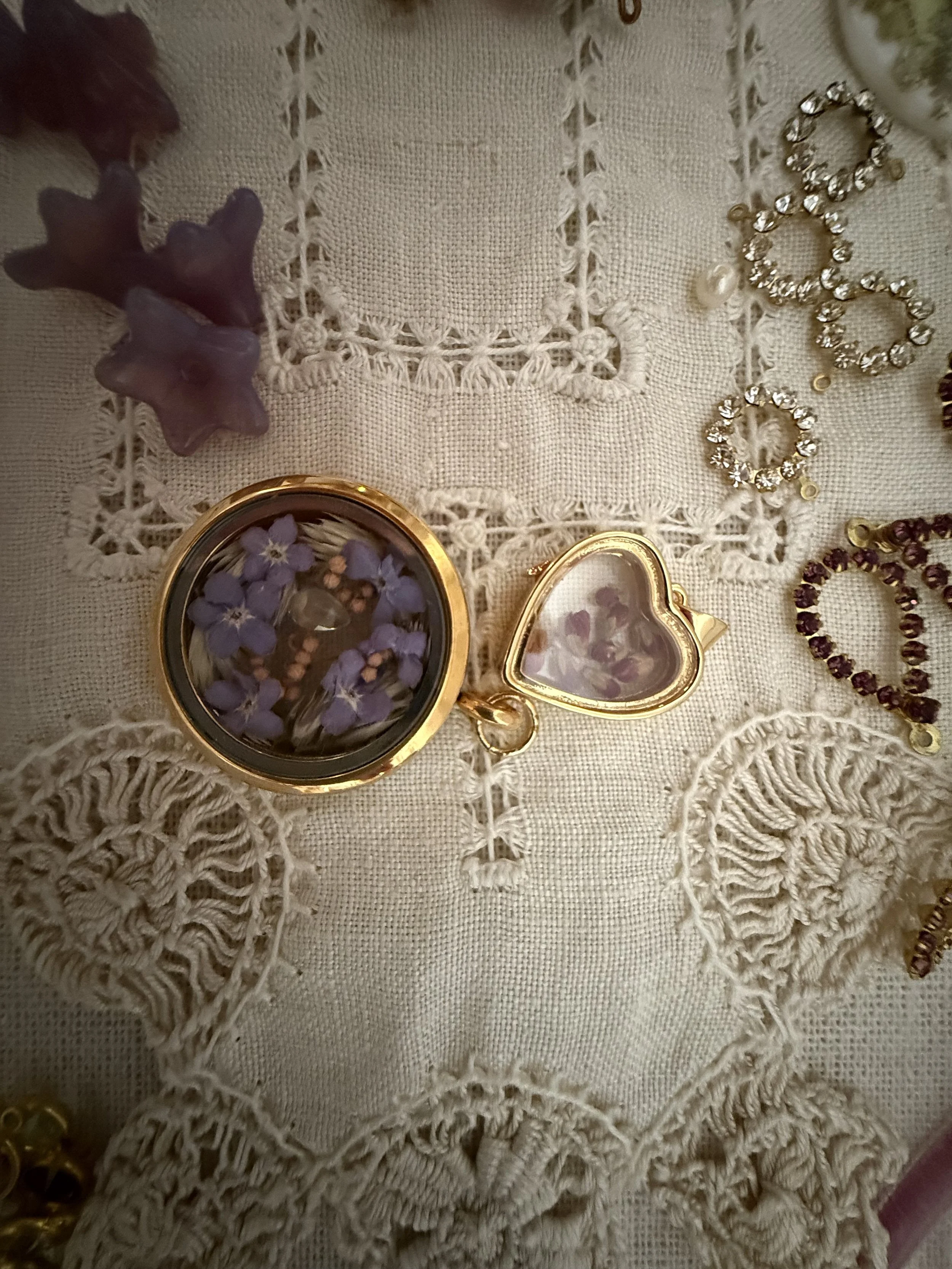 A collection of jewelry including earrings, a locket with purple flowers, and starfish-shaped ornaments, displayed on intricate lace fabric.