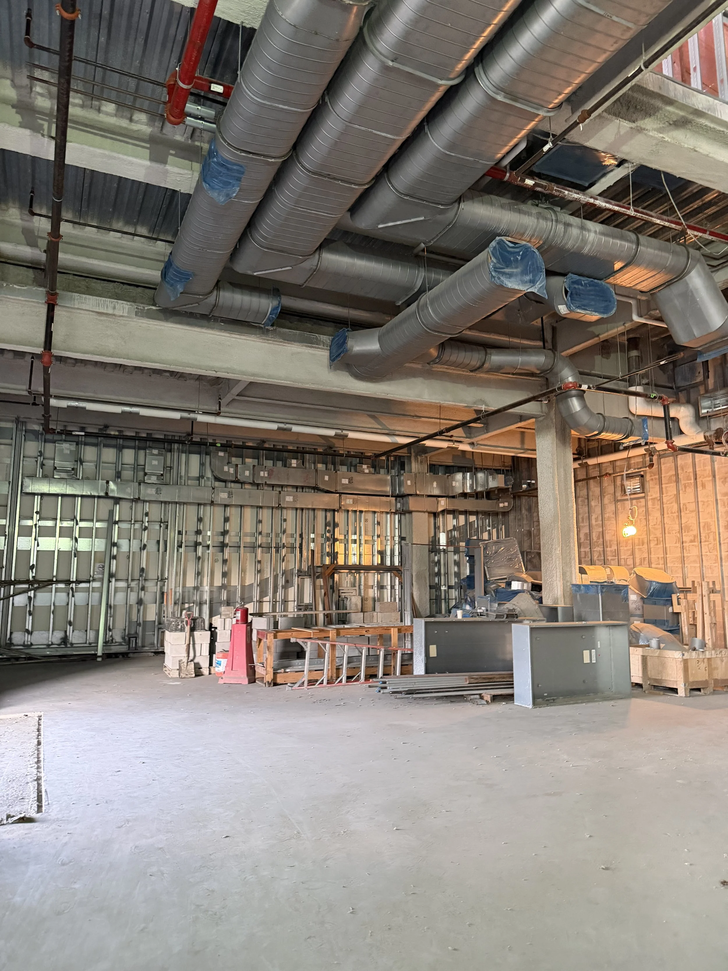 Construction site with exposed HVAC ductwork, unfinished walls, construction materials, and equipment.