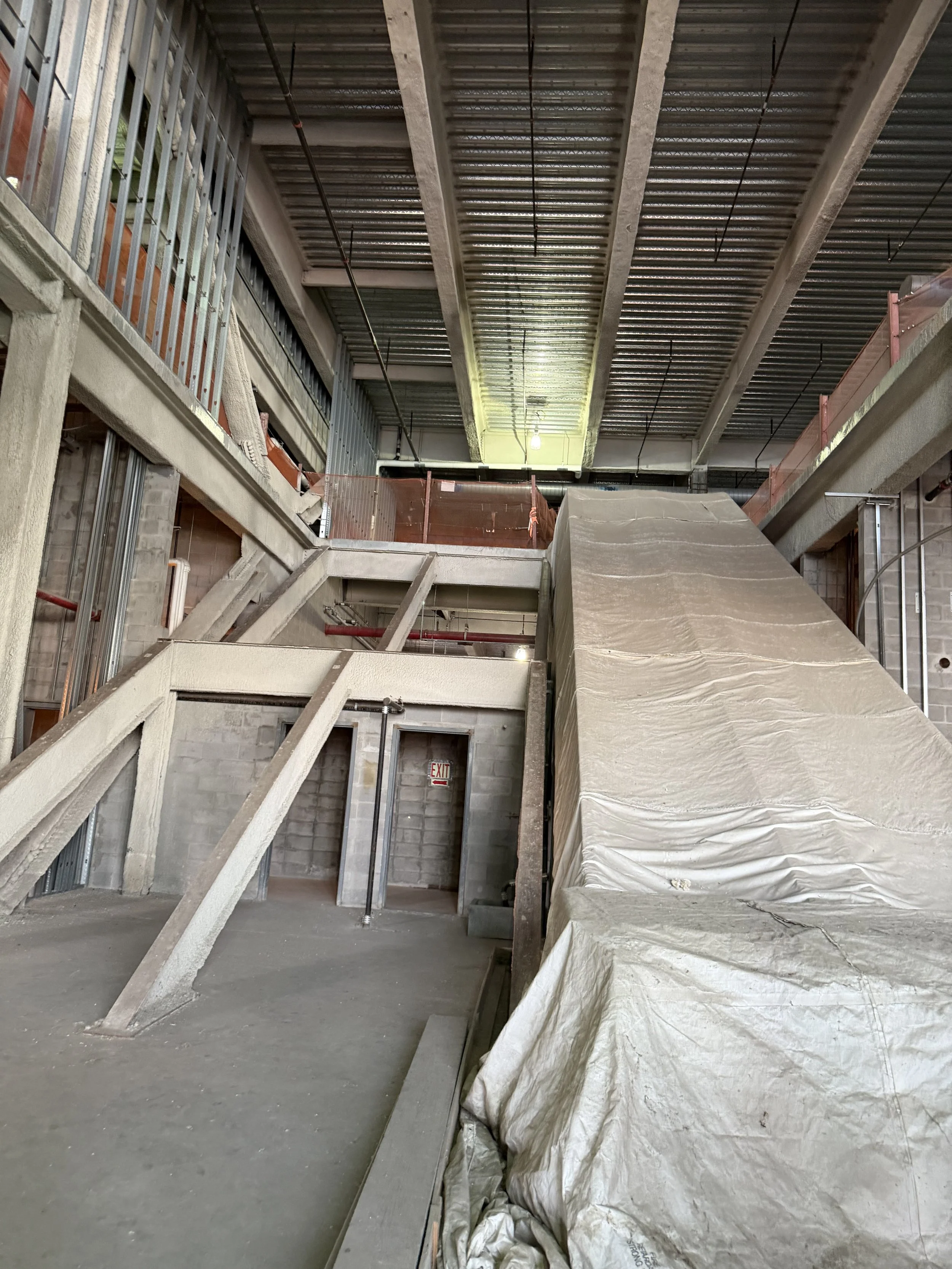 Interior of a building under construction with concrete stairs, metal railings, and a sloped covered area.