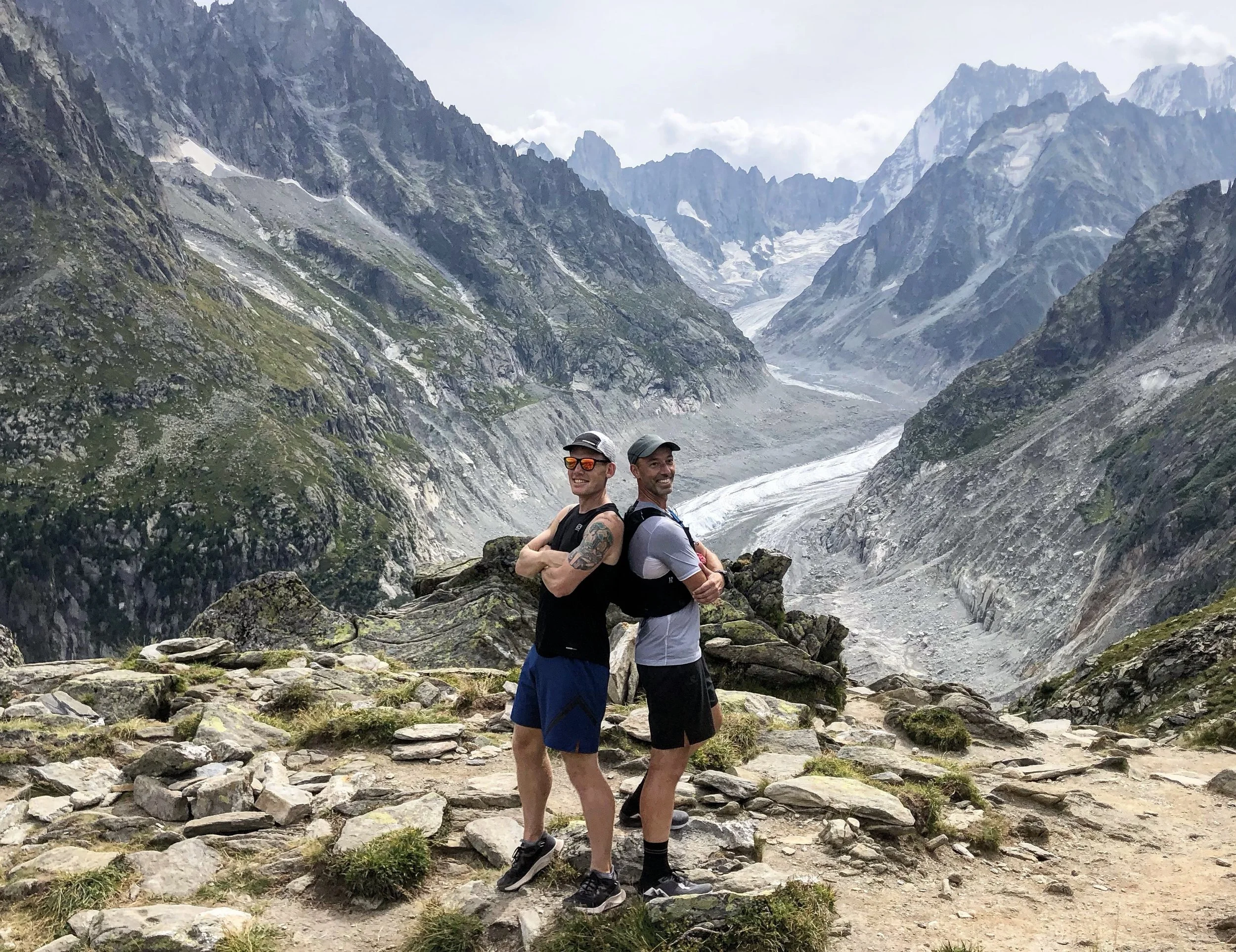 Owners Ed and Kyle posing back to back against scenic mountain backdrop, showcasing outdoor adventure lifestyle.