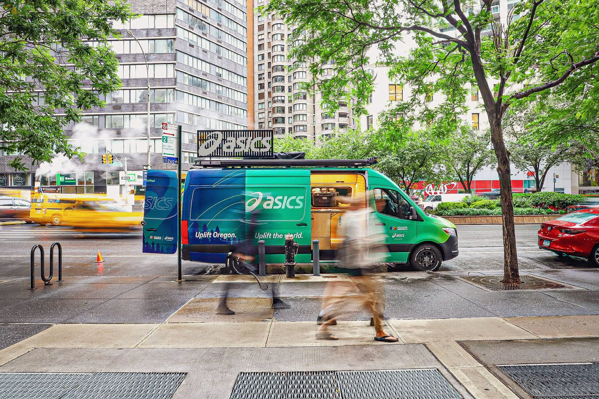 Blurry silhouettes of people walking past an Ascis Sprinter van in NYC, conveying a sense of bustling city life and movement.