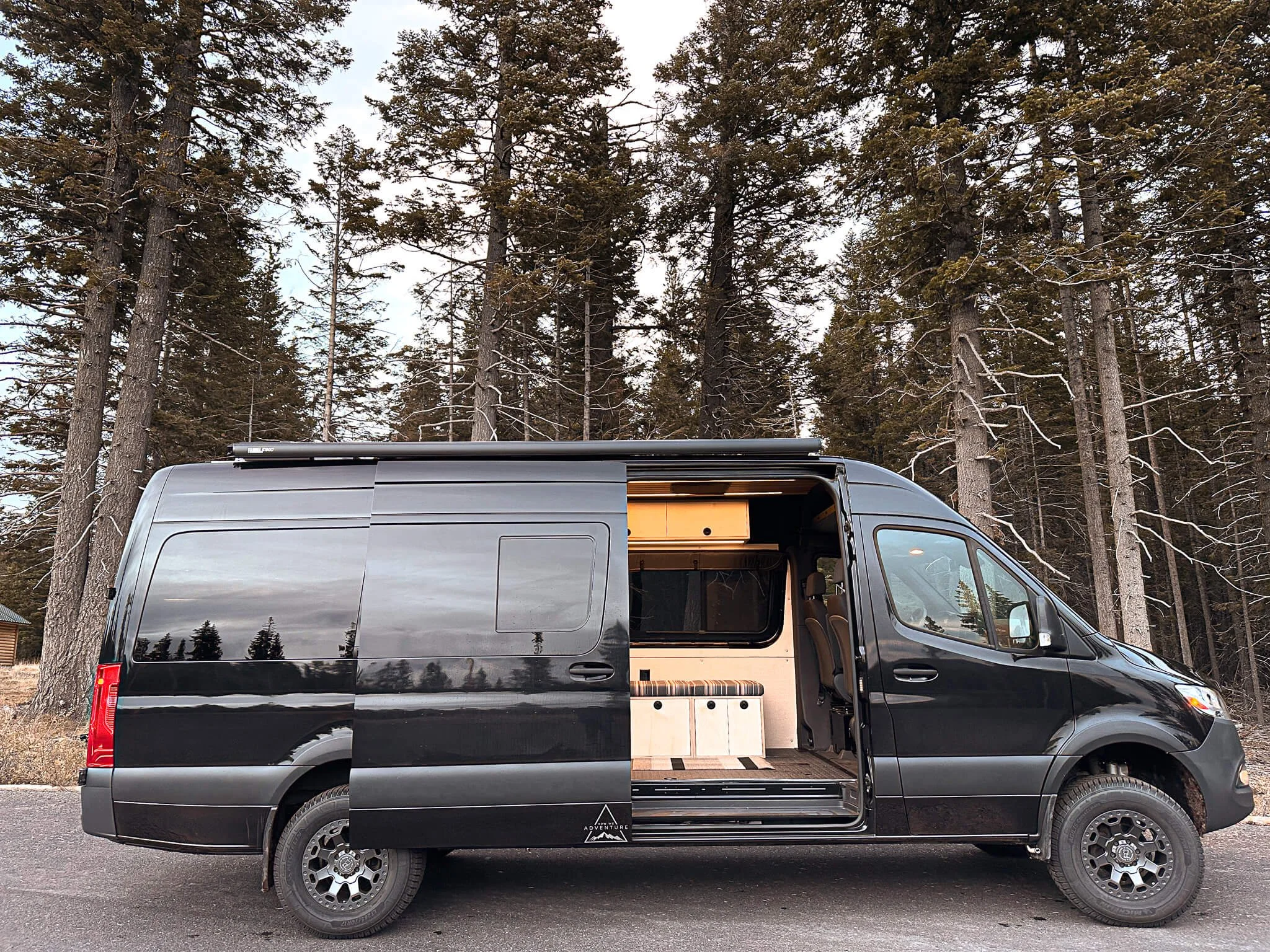 Open slider door revealing custom cabinetry and interior of 'Black Mamba' 170 Sprinter van.