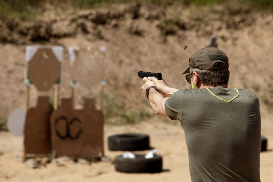 A shooter practicing pistol fundamentals at an outdoor range, brass ejecting mid-shot