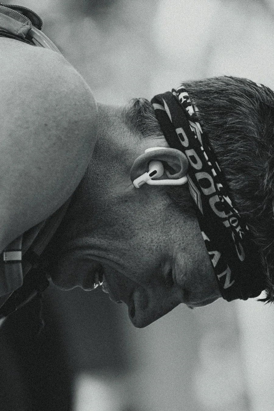 Close-up of a person wearing earbuds, with a headband and short hair, looking downward.