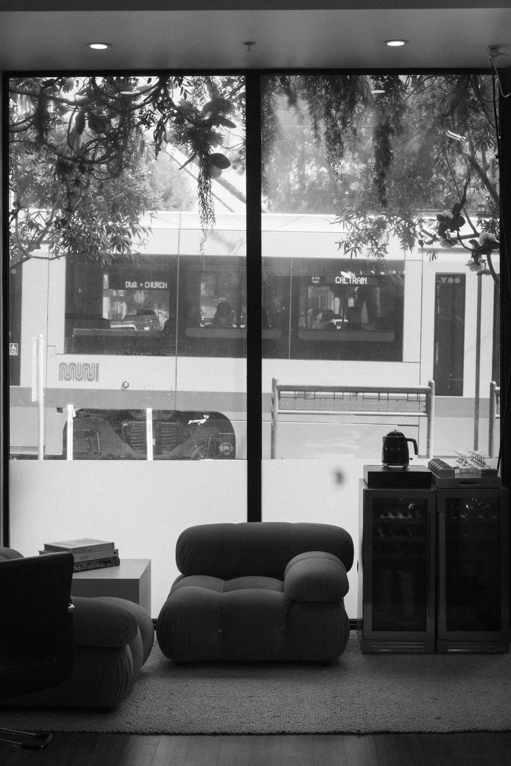 Me:
	Salon waiting area with a plush beige tufted lounge chair beside a small side table stacked with books, in soft natural light.



Me:
Black-and-white photo of the salon lounge, a chair silhouetted against floor-to-ceiling windows overlooking the