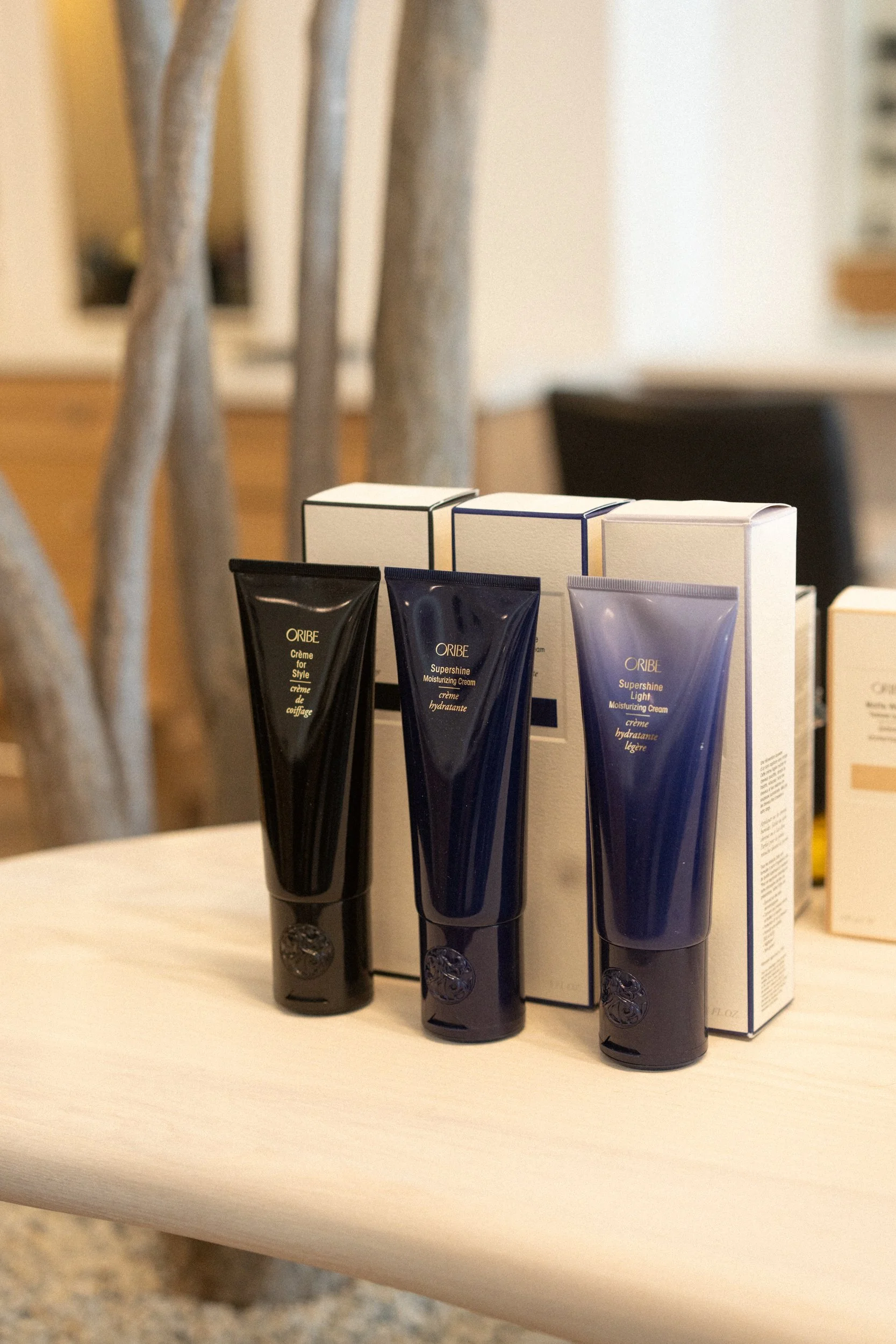 Oribe hair products- dark navy styling tubes lined up on a light counter, with product boxes standing behind them.