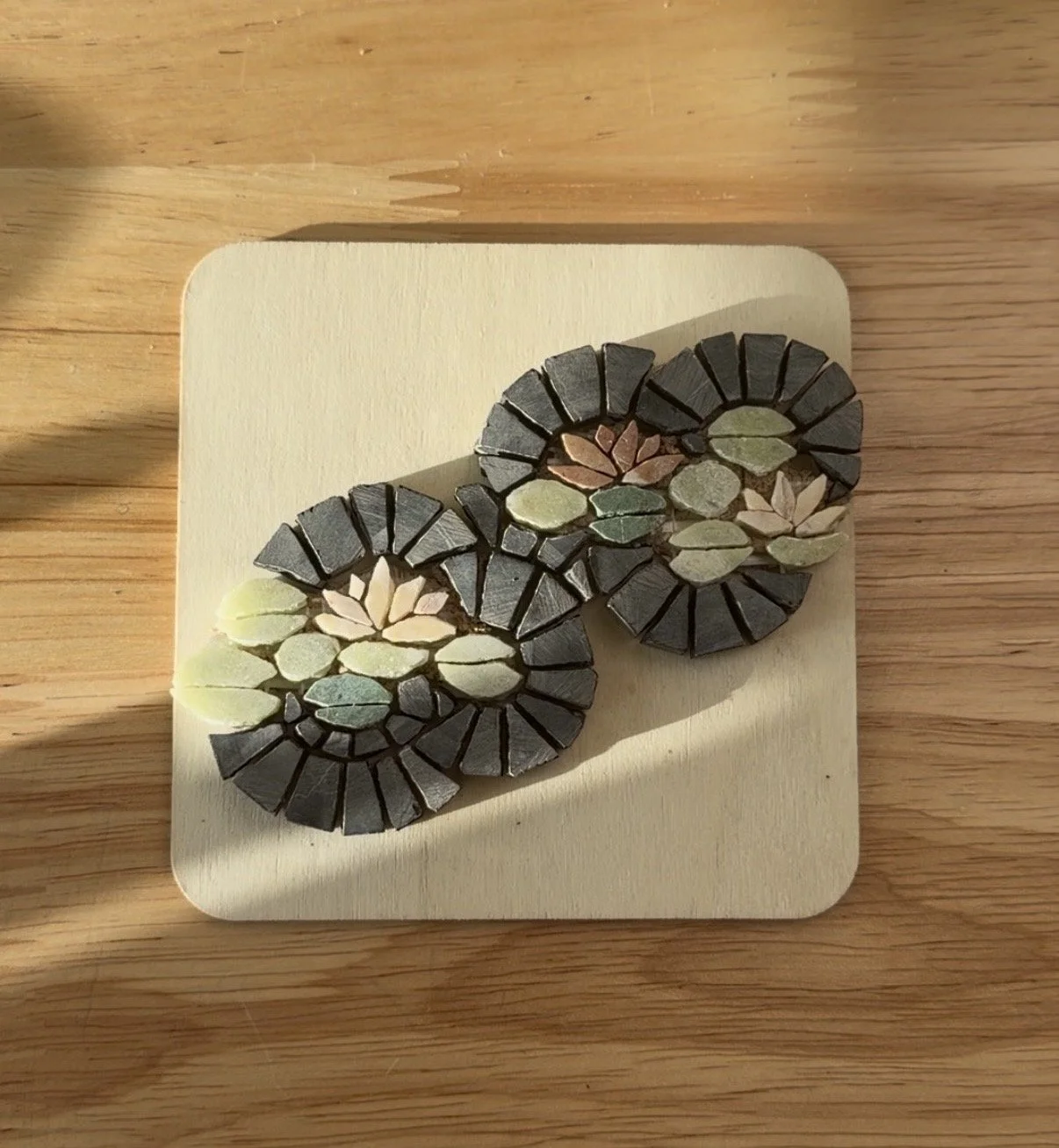A decorative mosaic piece made of colorful stones arranged in a pattern on a wooden base.