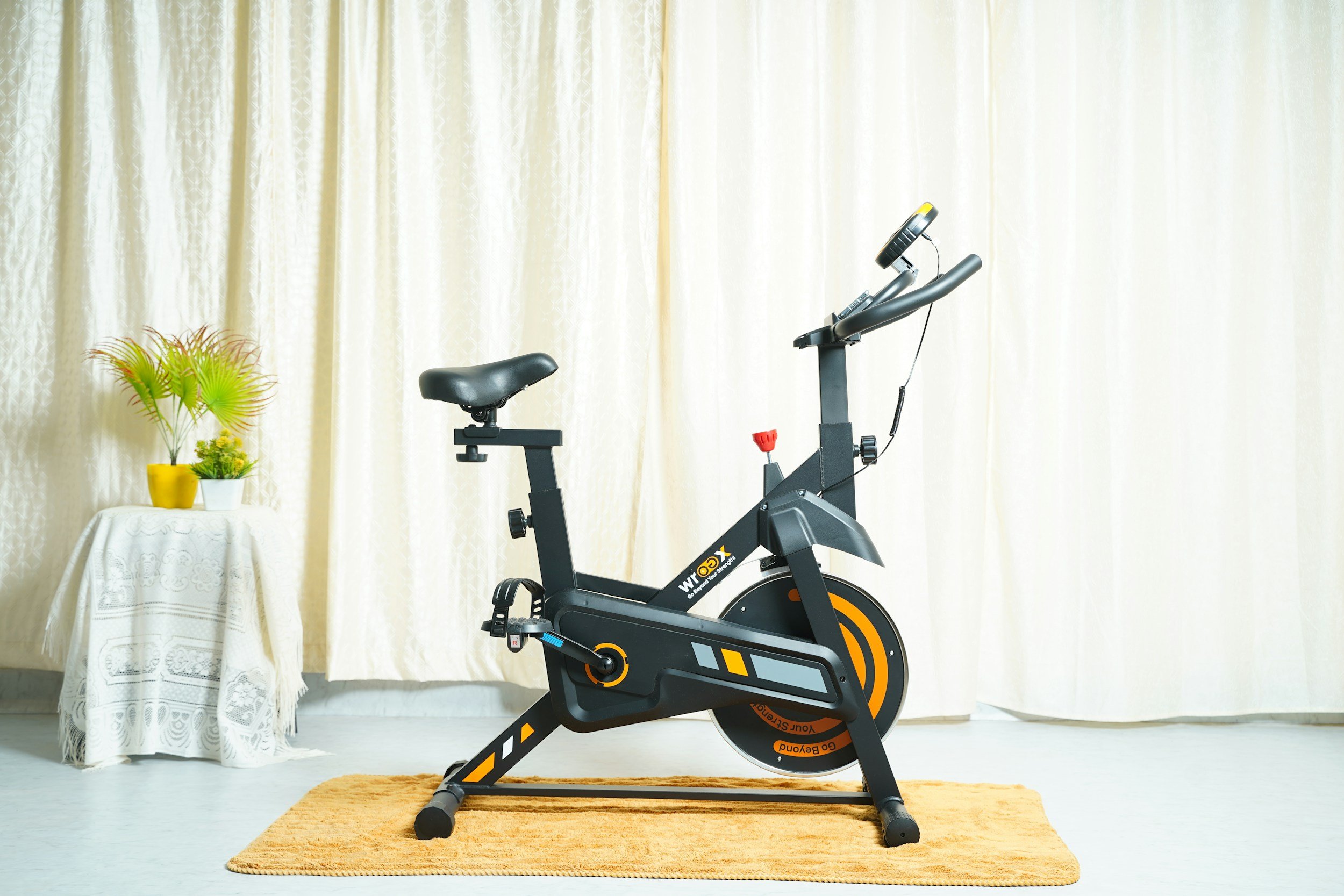 A group of women exercising on stationary bikes in a gym or fitness class, with a plain brick wall in the background.