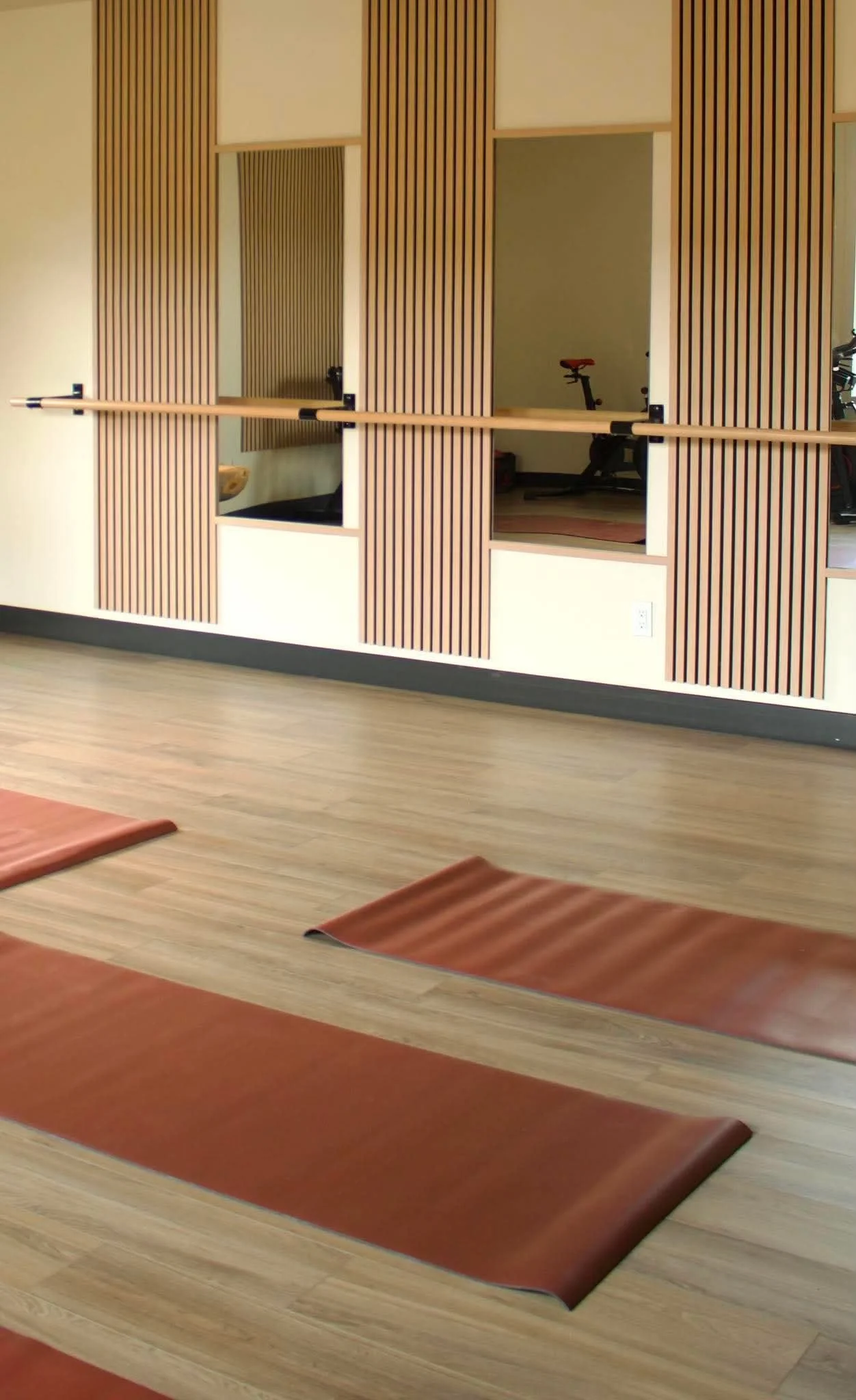 Yoga studio with wooden wall, mirrored window, and yoga mats on wooden floor.