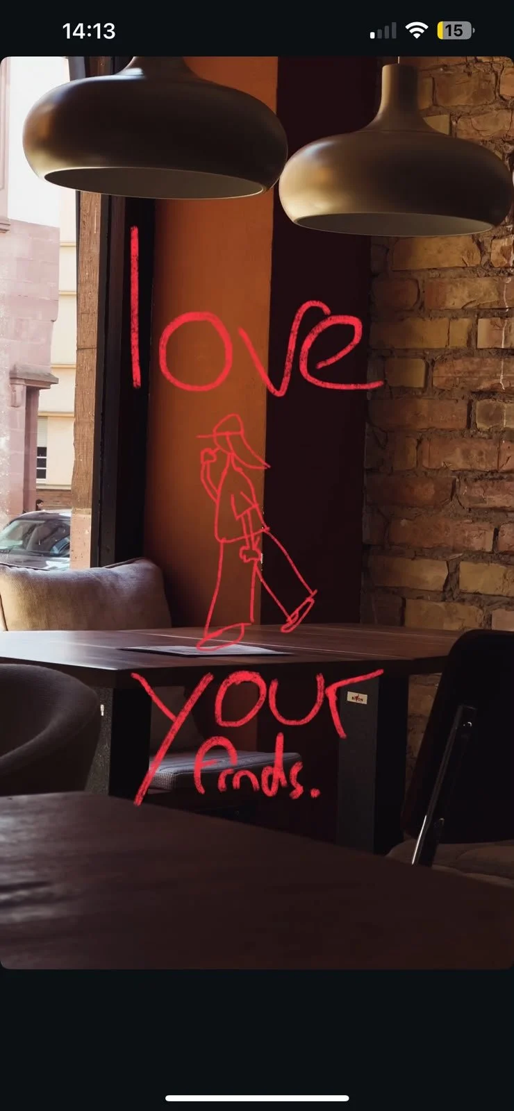 Ein Fenster mit einem Neon-Schriftzug, der 'love your' und eine gezeichnete Person beim Staubsaugen zeigt, im Innenraum eines Cafés oder Restaurants mit Holz- und Steinelementen.