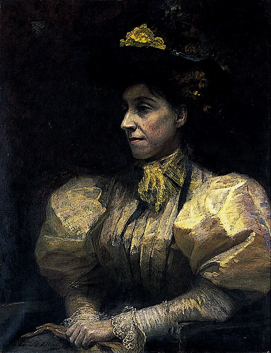 Portrait of Catherine Maude Nichols in vintage clothing and a large hat with a yellow flower, sitting with her hands folded, in a dark setting.
