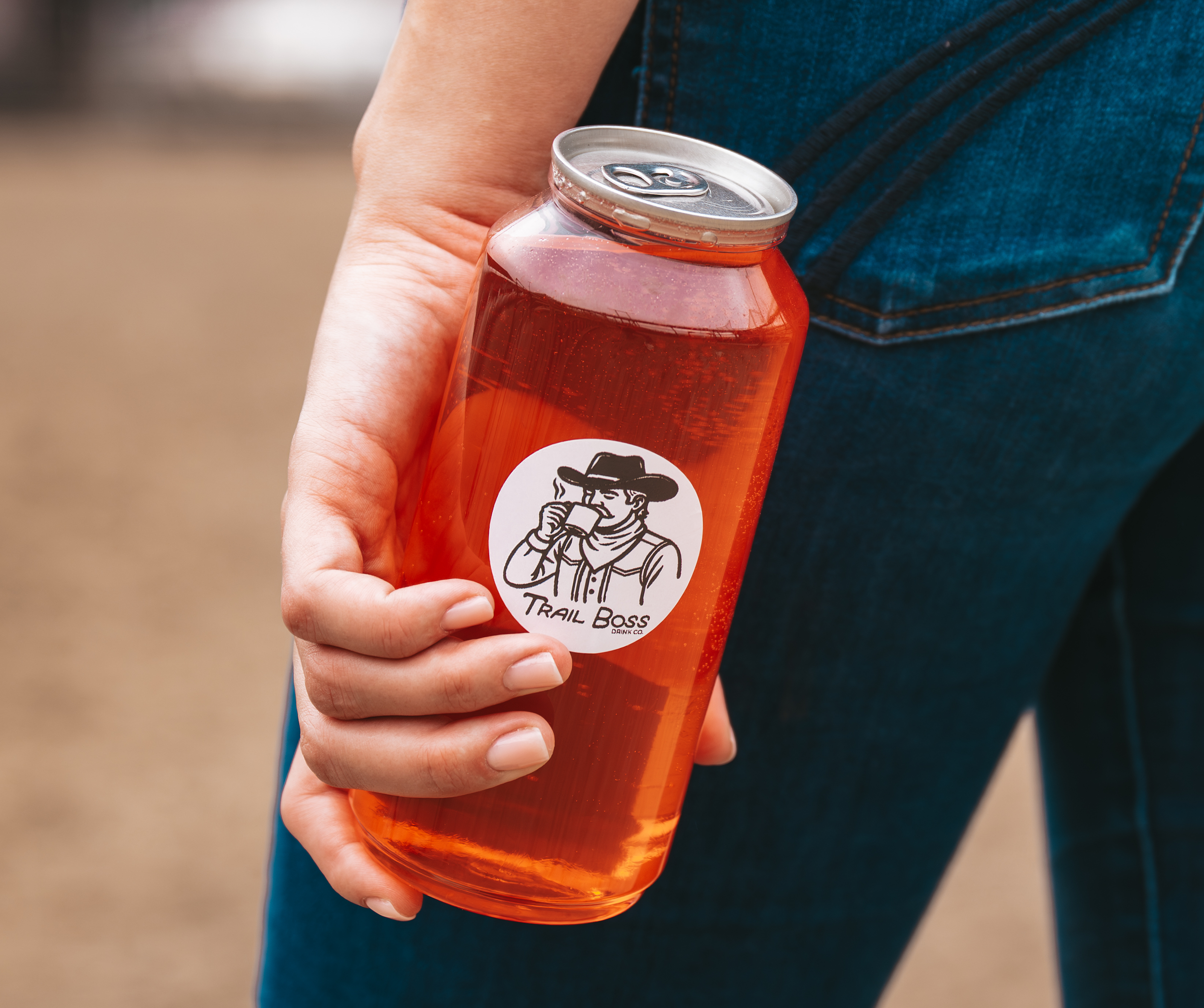 A person holding a can of orange soda behind their back, wearing a blue denim shirt.