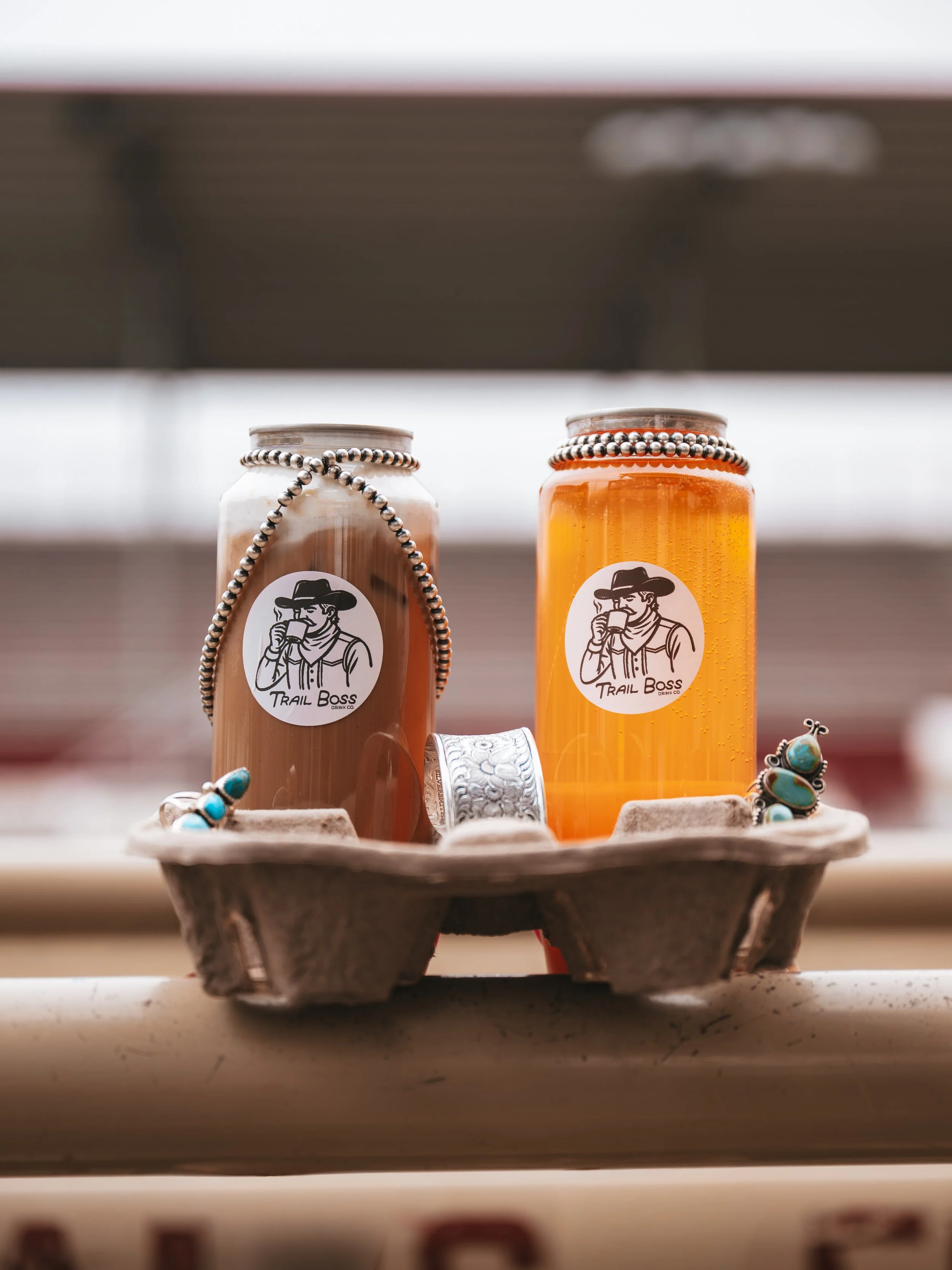 Two cans of beverages on a wooden tray, decorated with jewelry and rings, with a blurred background.