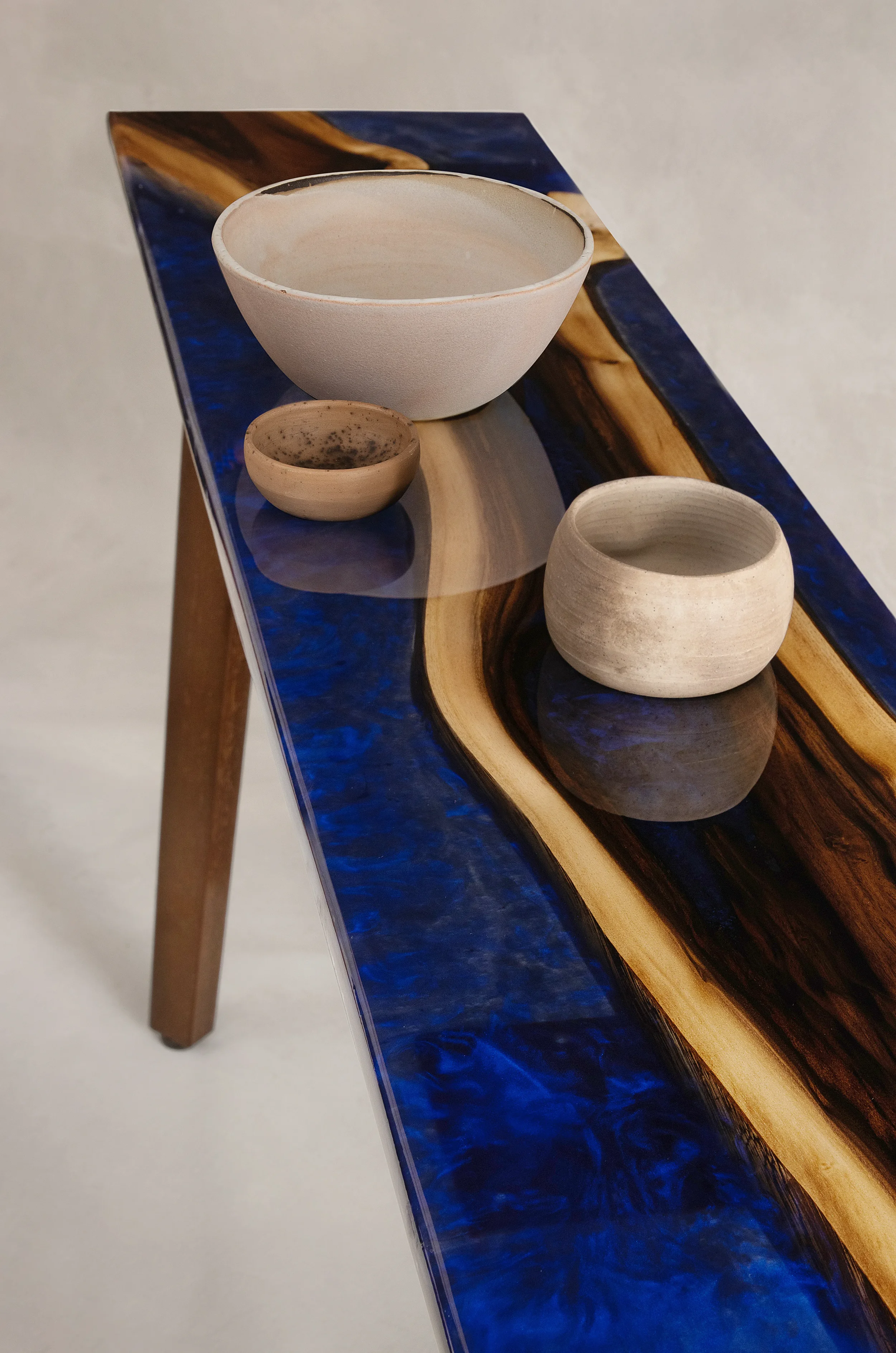Three ceramic bowls of varying sizes and colors are arranged on a wooden and resin table with a swirling blue and tan pattern.