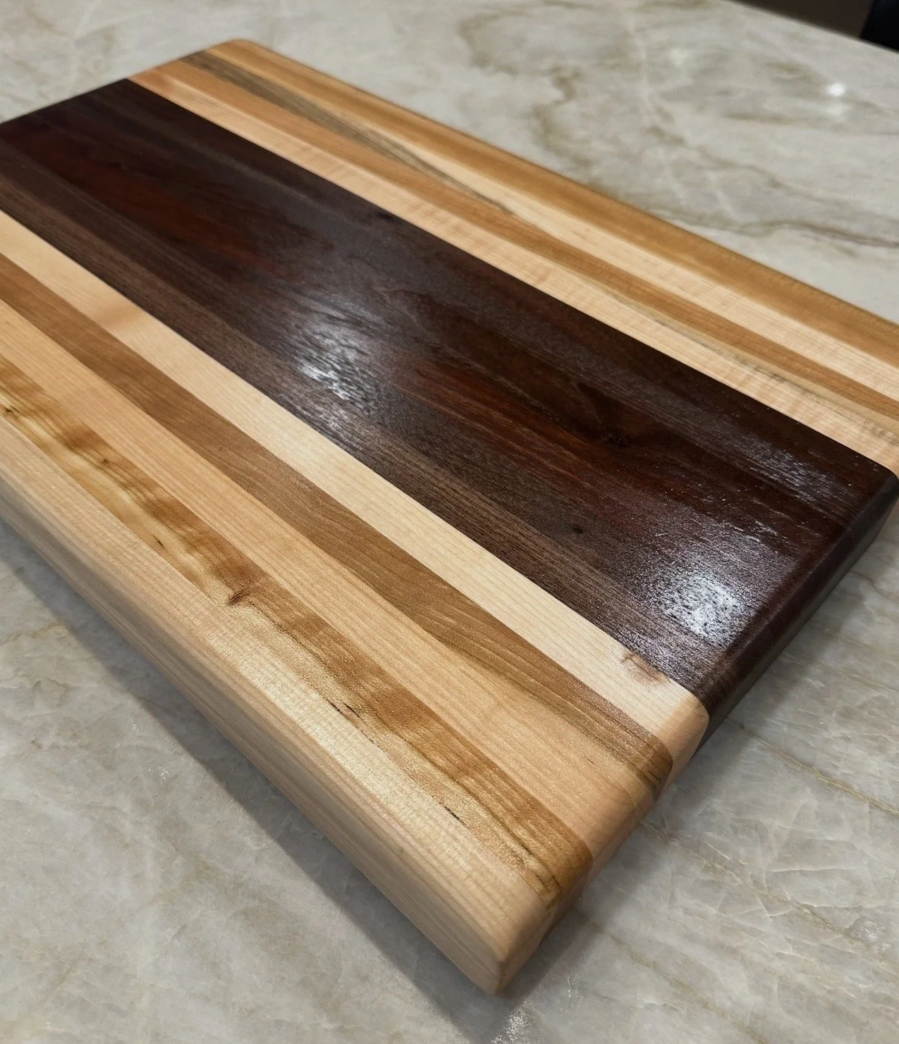A wooden cutting board with a handle, a small bowl with a wooden spoon containing salt or sugar, a pair of small scissors, and a pot with purple flowers and green leaves on a light-colored surface.