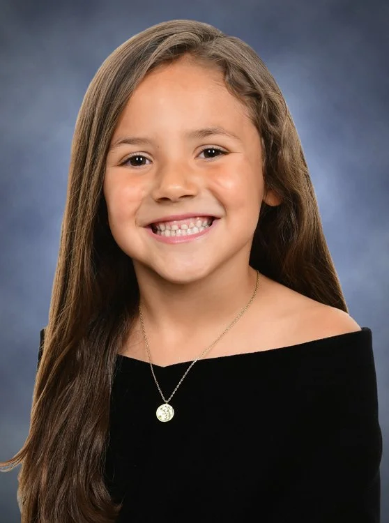 Smiling child wearing a black velvet drape for a school portrait