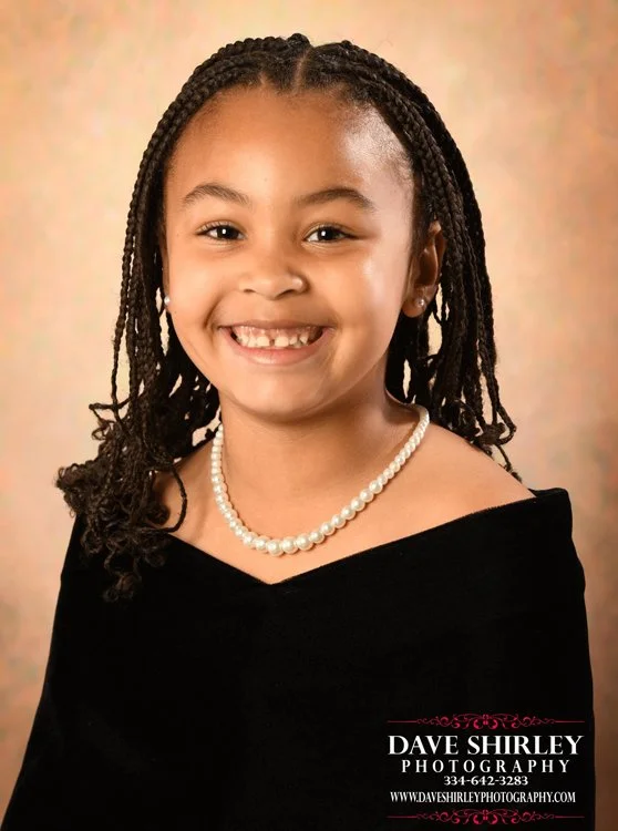 Preschool student wearing a child-size black velvet portrait drape