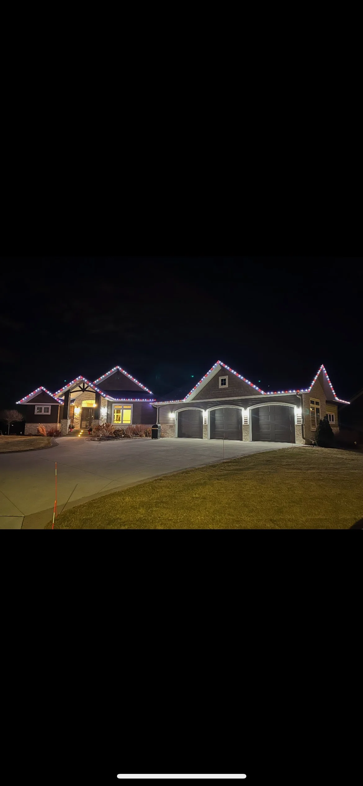 Single-story home at night with permanent roofline lighting in red, white, and blue
