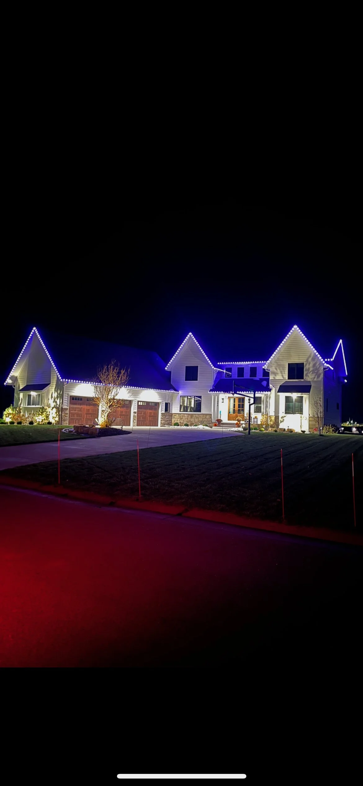 Large white home at night with warm white permanent roofline lighting and blue accent lighting on the gables