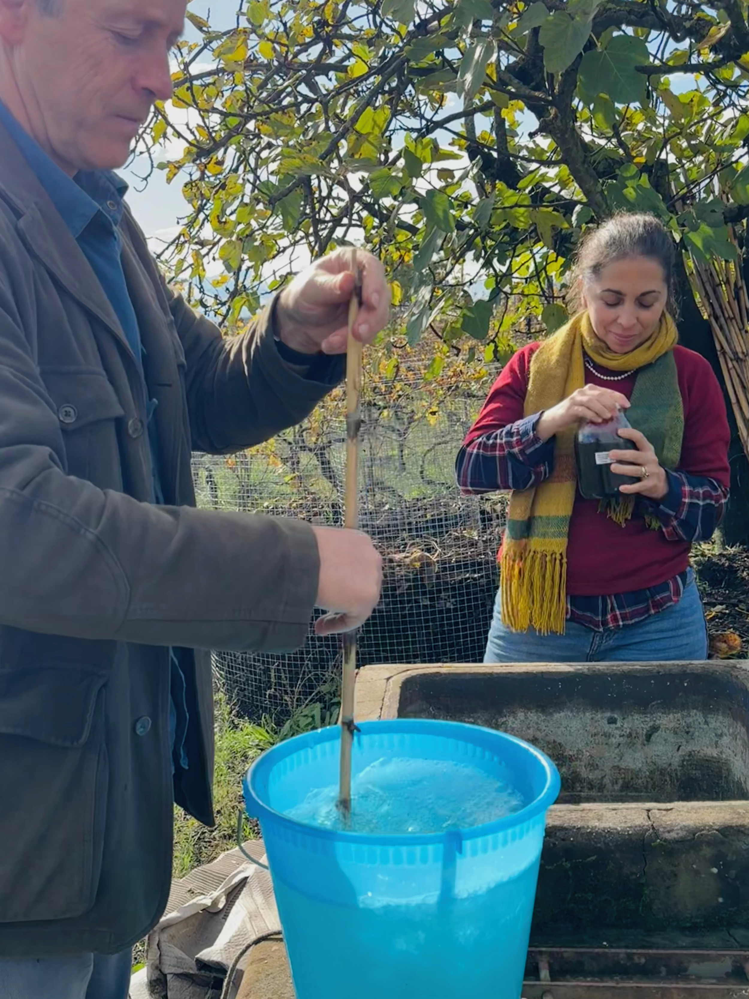 Winemakers Maria Ernesta Berucci and Geminiano Montecchi preparing rainwater and mushroom tea for use in biodynamic viticulture in Piglio, Lazio, Italy. They are surrounded by greenery and trees.