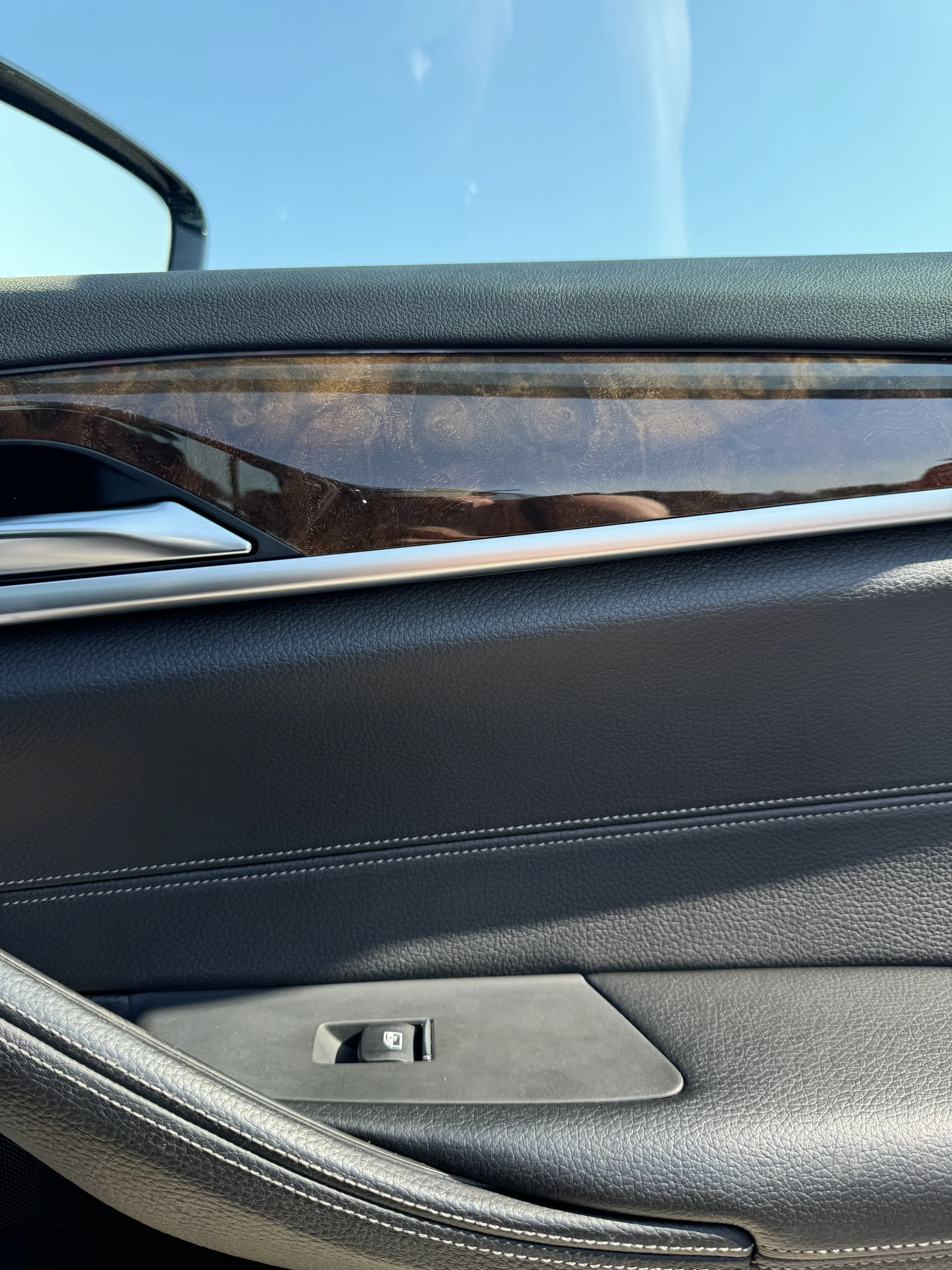 Close-up of the interior of a car door, showing the window, lock switch, and textured black upholstery with stitching.