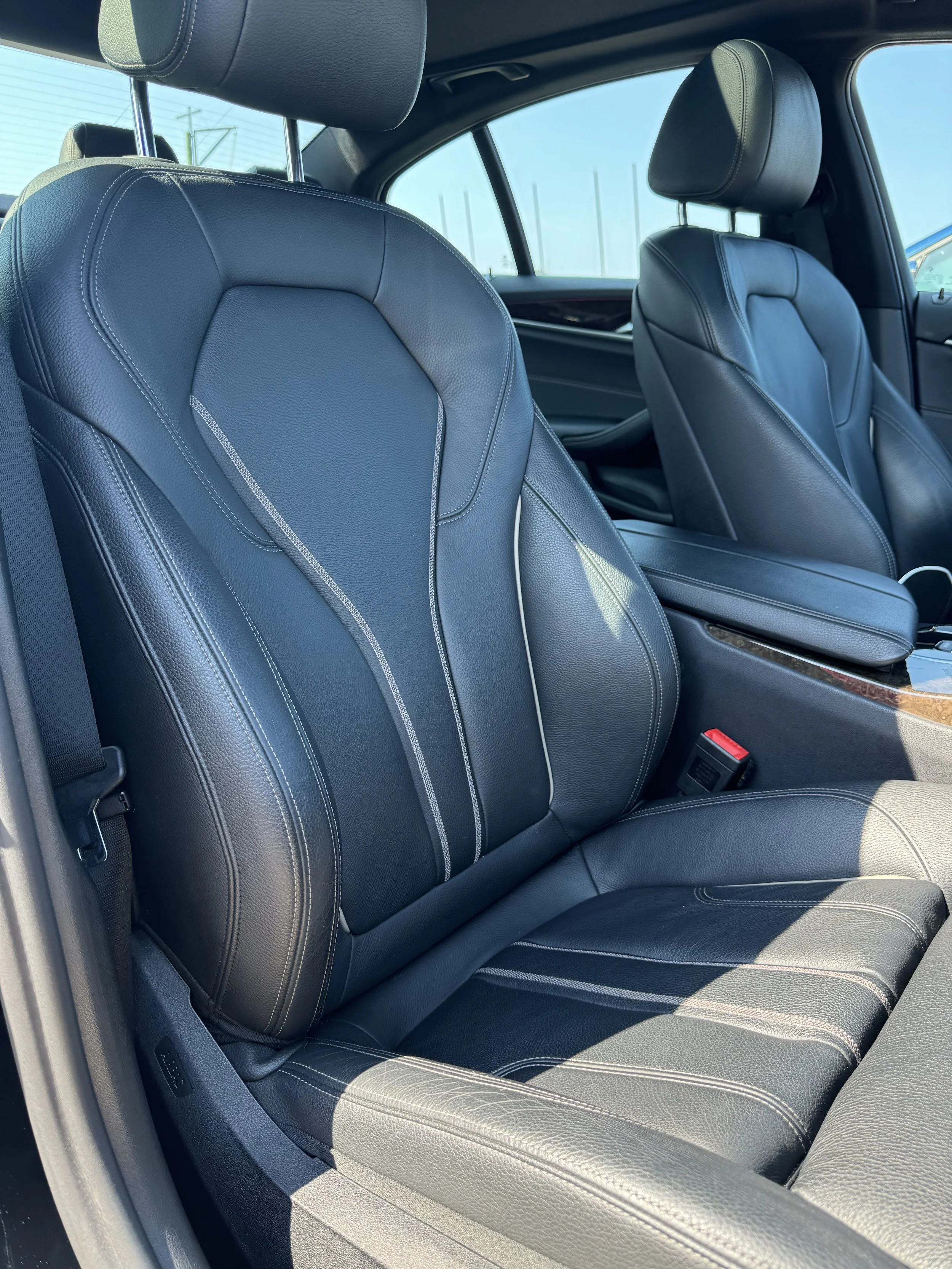 The interior of a car featuring black leather seats with white stitching, headrests, and a view of the side window and dashboard.