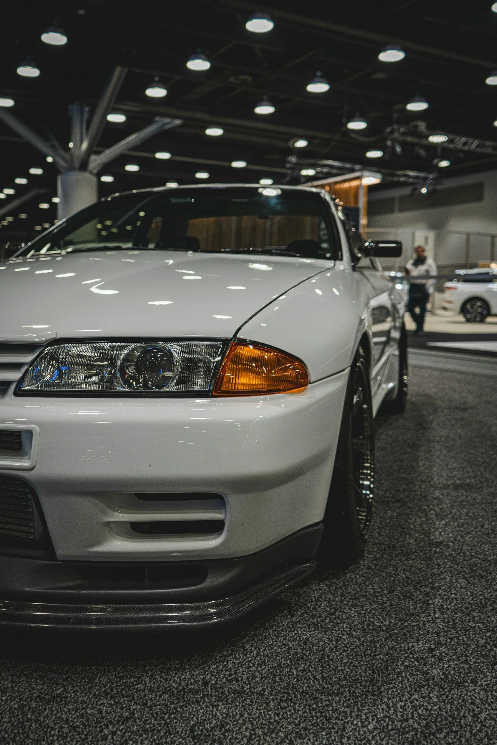 Close-up of a white car with a black front splitter on display at an indoor car show.