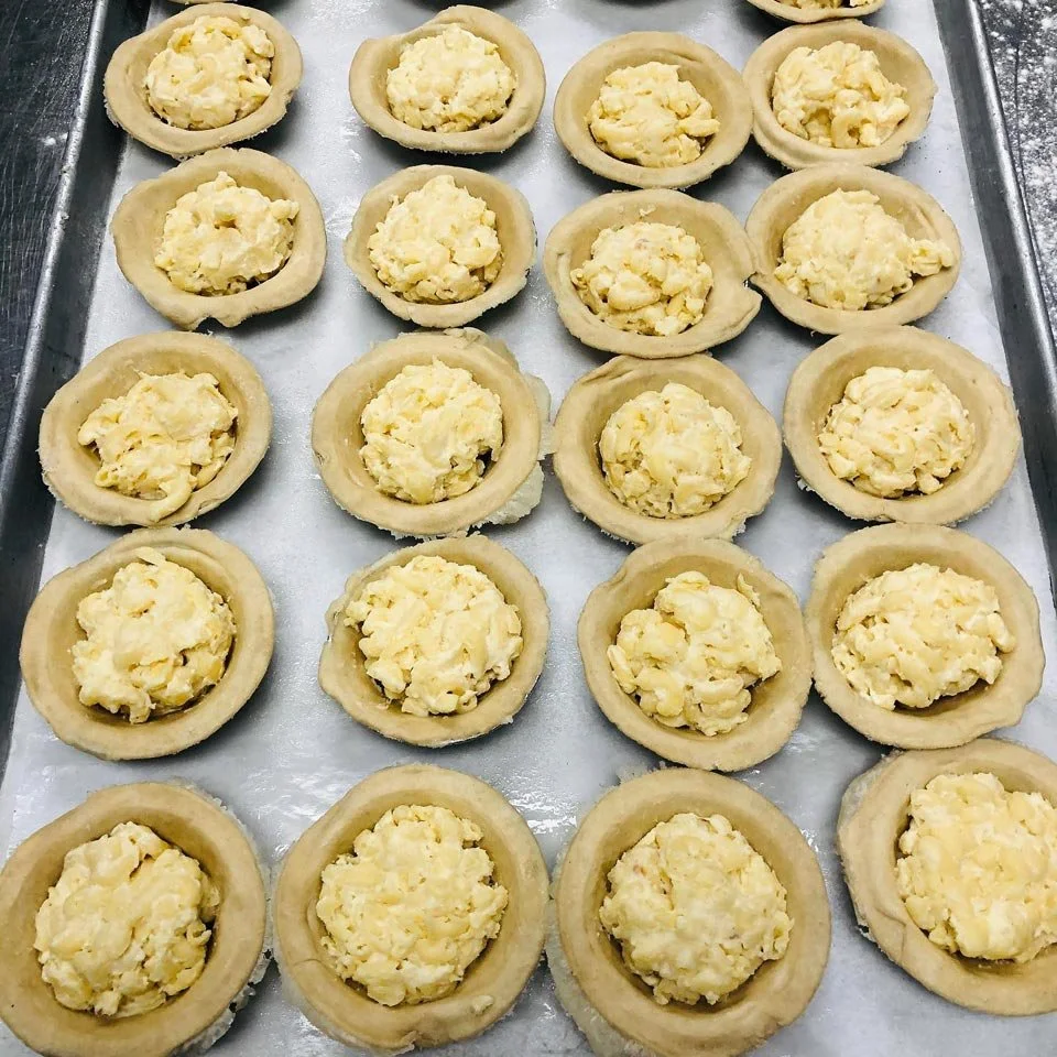 Baking sheet with unbaked mini tarts filled with scrambled eggs.