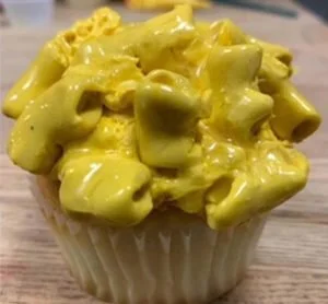 A cupcake topped with a yellow frosting resembling melted cheese and chunks of what appears to be cheese.