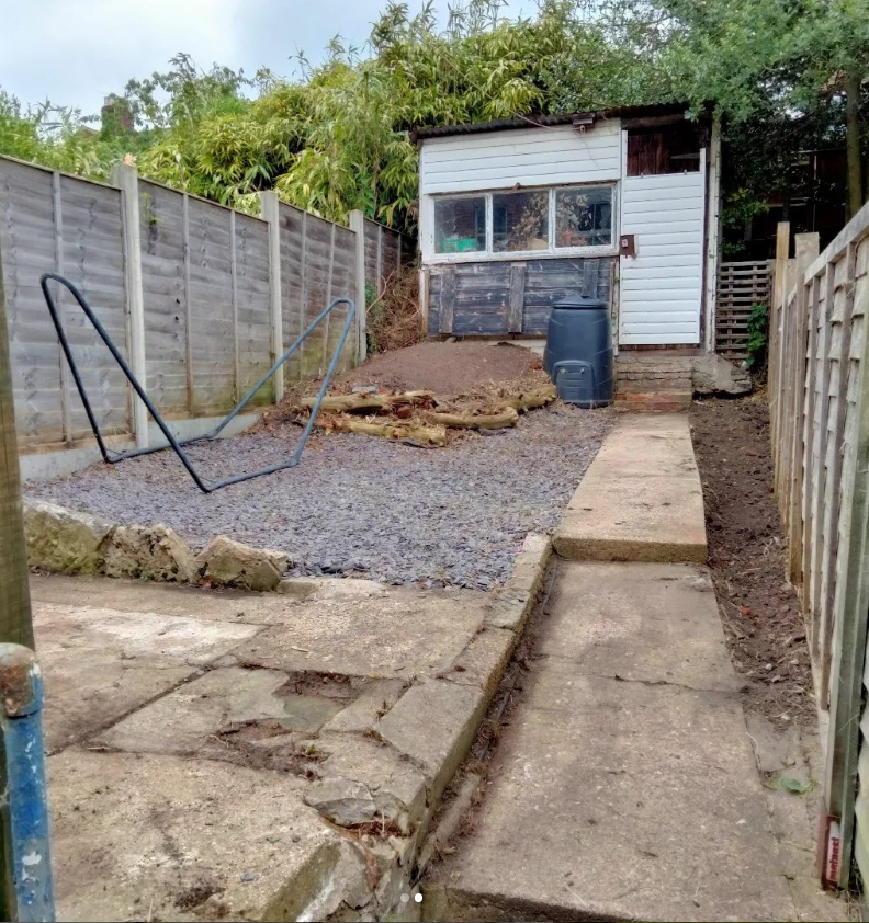 Backyard with a small shed, gravel and concrete pathway, and a black compost bin.