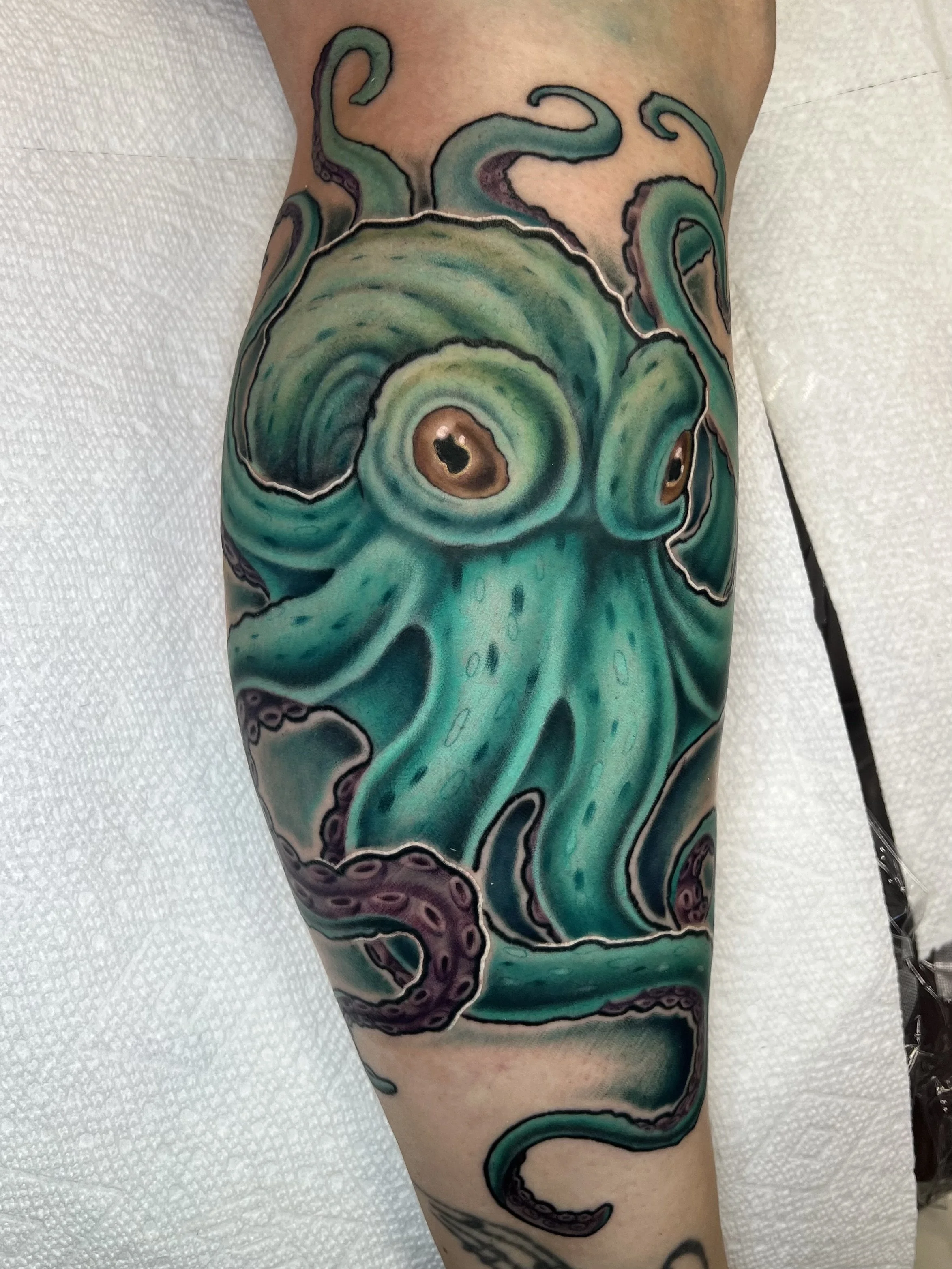 Colorful octopus tattoo on person's leg, featuring green and purple hues with detailed suction cup textures.
