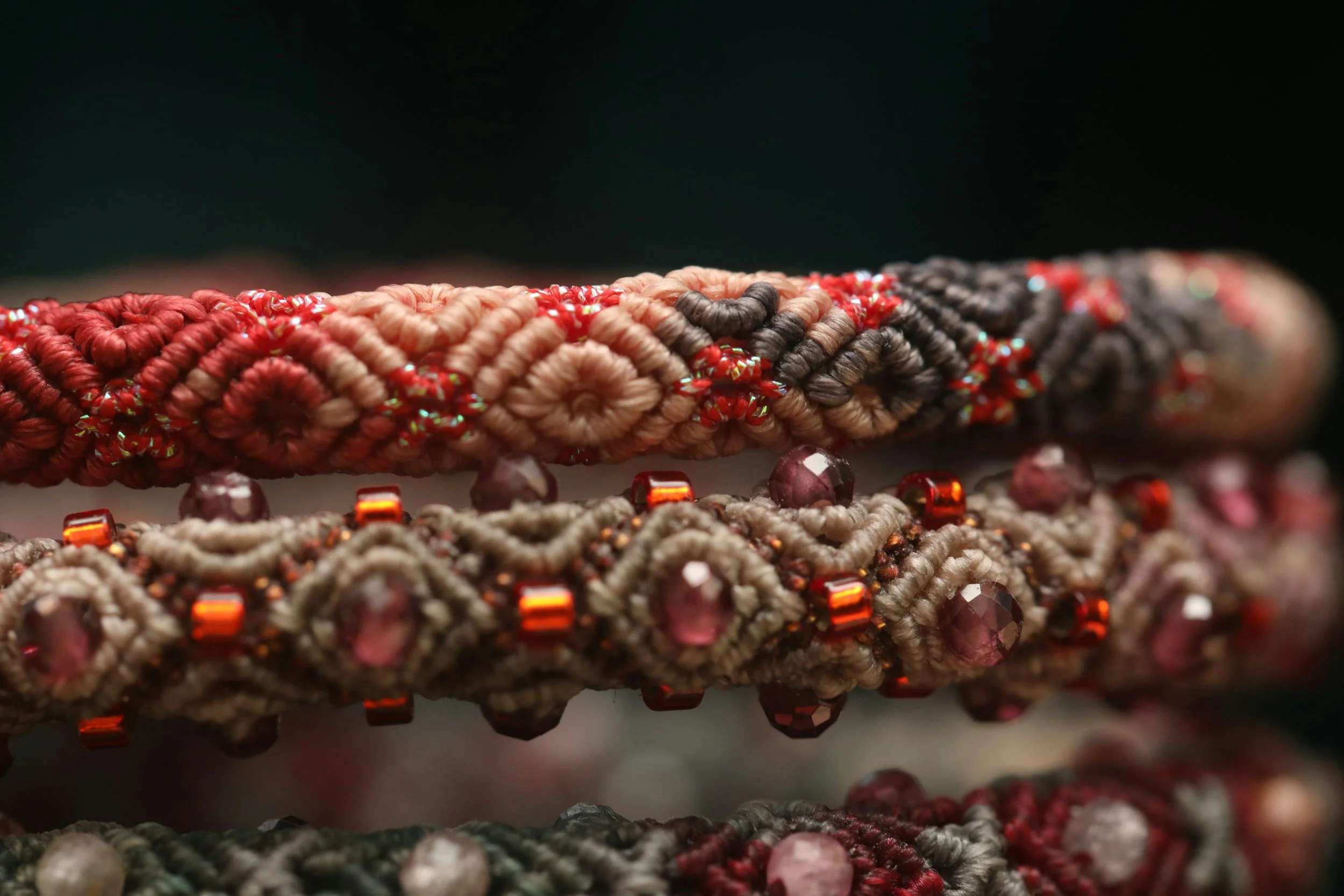 Close-up photo of an array of intricately woven bracelets with beads, yarn, and thread, laid out on a flat surface against a dark background.