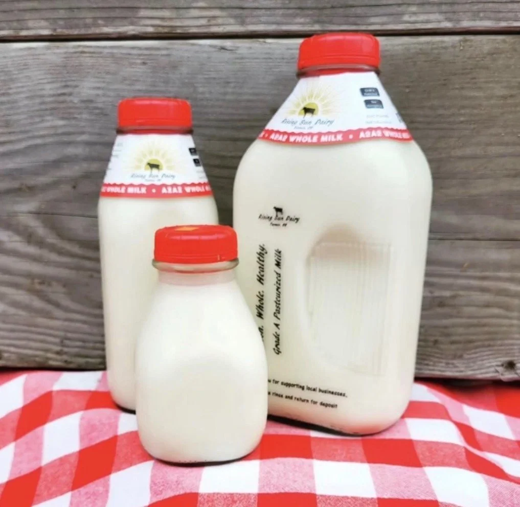 Three bottles of whole milk with red caps on a red and white checkered cloth, with a wooden background.