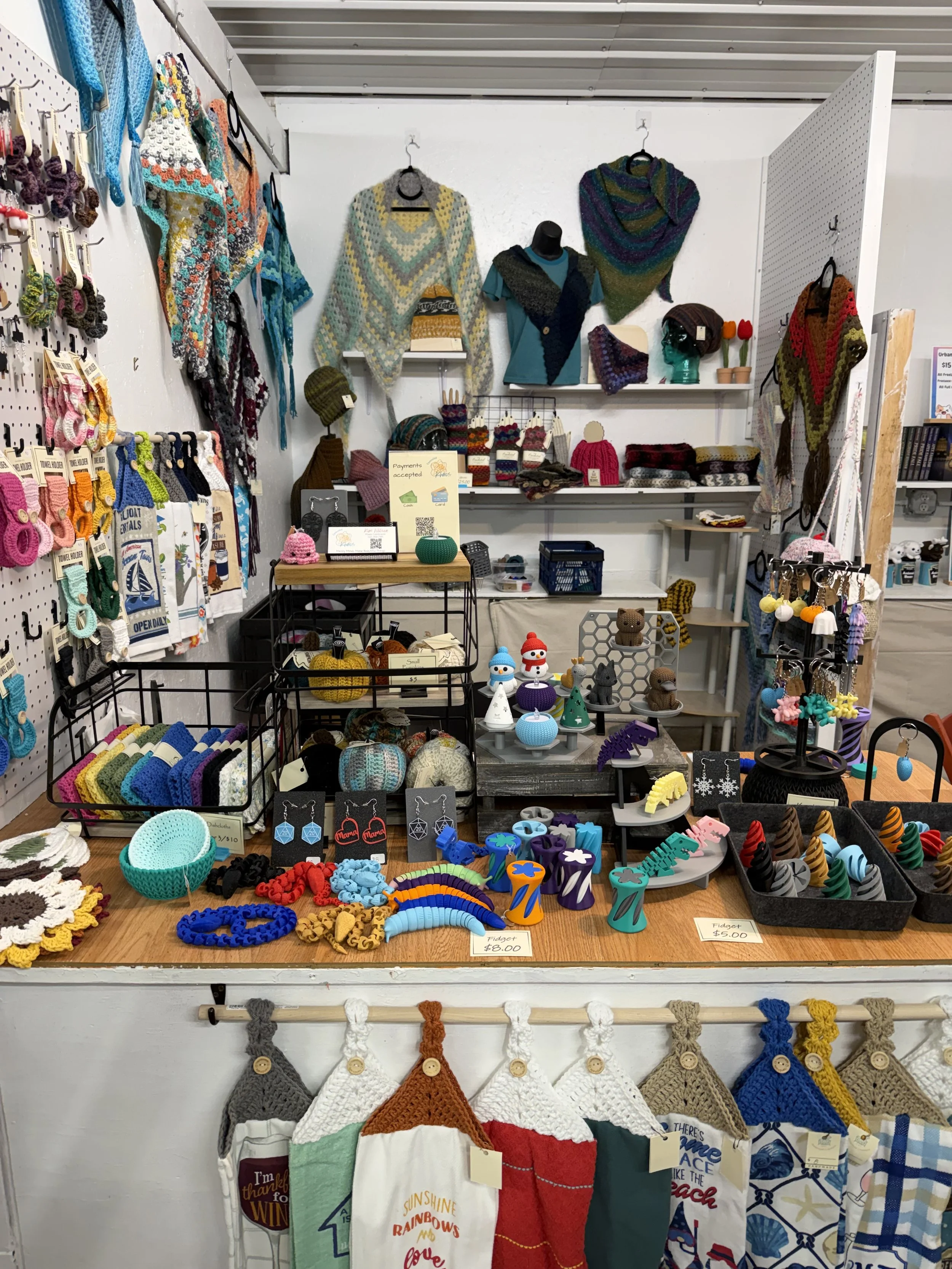 Display of colorful handmade crocheted hats, scarves, and accessories in a craft market booth.
