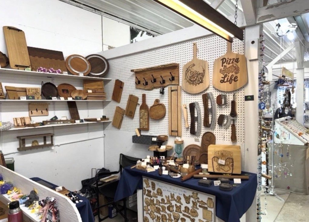 A display of wooden crafted items, including cutting boards with engraved designs, hooks, and decorative pieces, arranged on shelves and a table in a store.