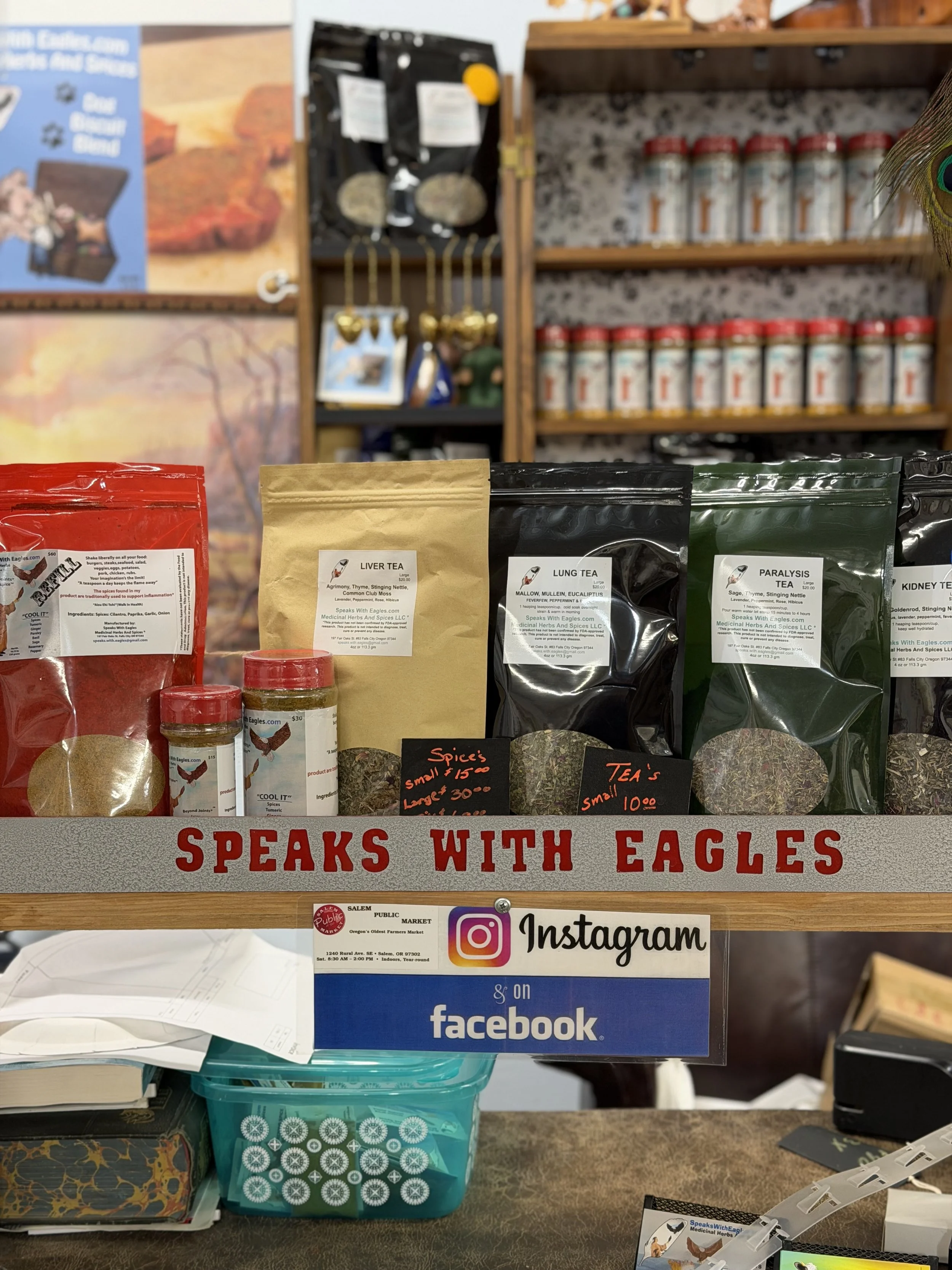 Shelf display with herbal tea bags, including Liver Tea, Lung Tea, Paralyze Tea, and Kidney Tea, with handwritten price signs and a decorative sign reading 'Speaks with Eagles'.
