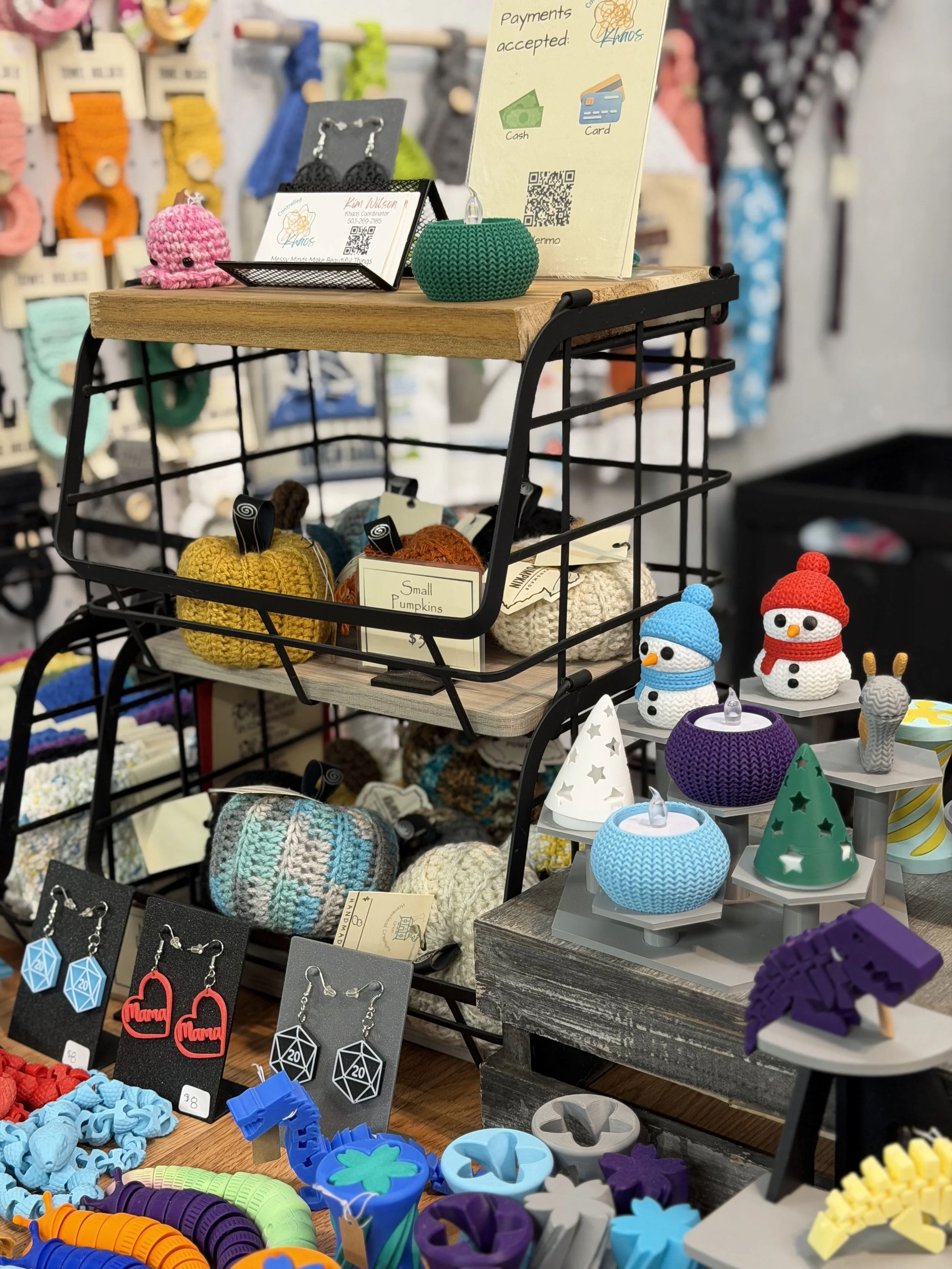 Display of various handmade crochet and knit items including pumpkins, snowmen, hats, and accessories at a craft fair or store.