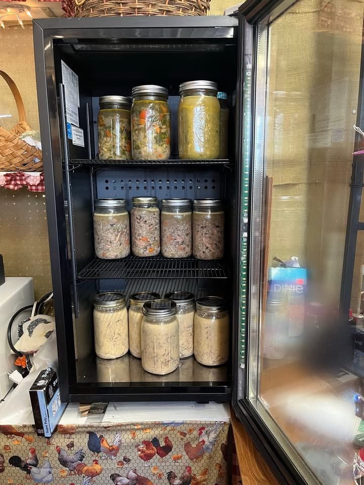 A black refrigerator with a glass door containing several mason jars filled with preserved foods on three shelves.