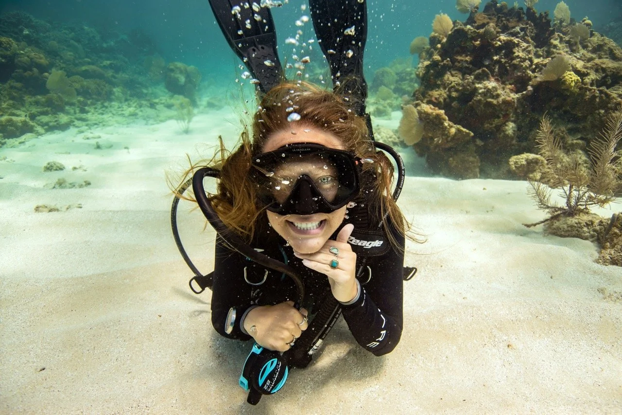 female scuba diver smiling at the camera with regulator out of her mouth under water
