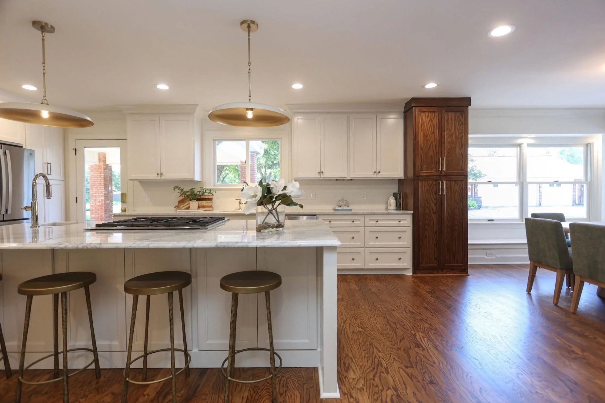 Open-concept kitchen with white cabinets, a marble island, a metal pendant light, and a view of living room windows with a dining area.