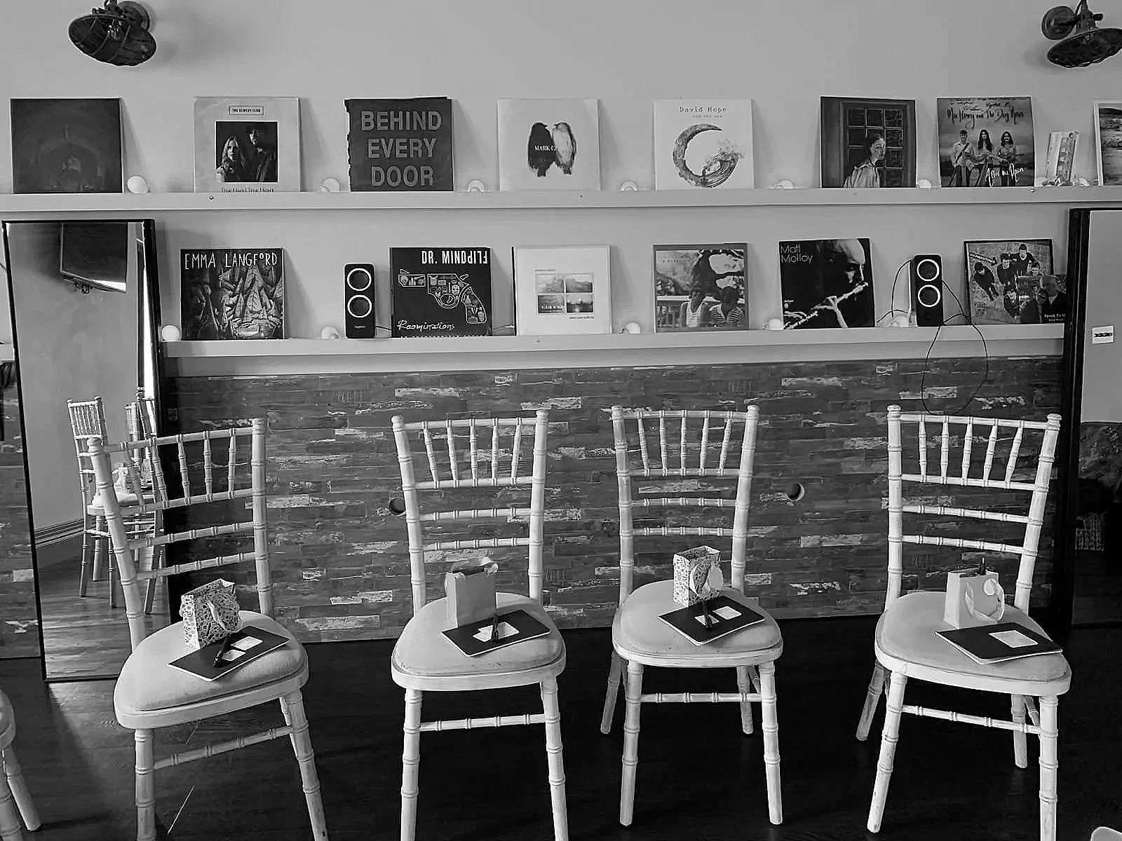 Empty chairs with napkins and plates set up in front of a bar with music records on shelves and framed pictures on the wall behind.