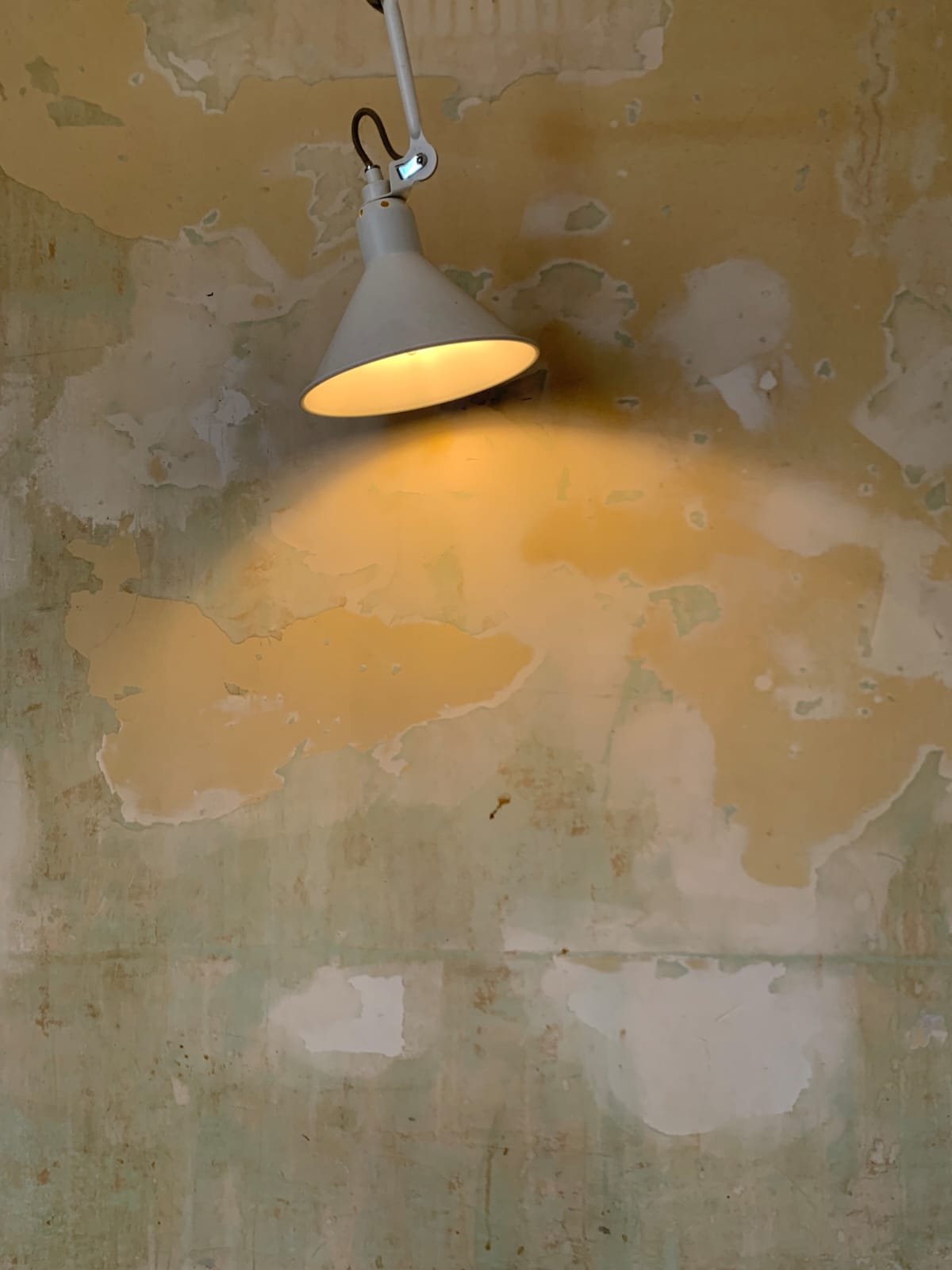 A white wall-mounted lamp casting warm light on a peeling, textured yellow and beige wall.