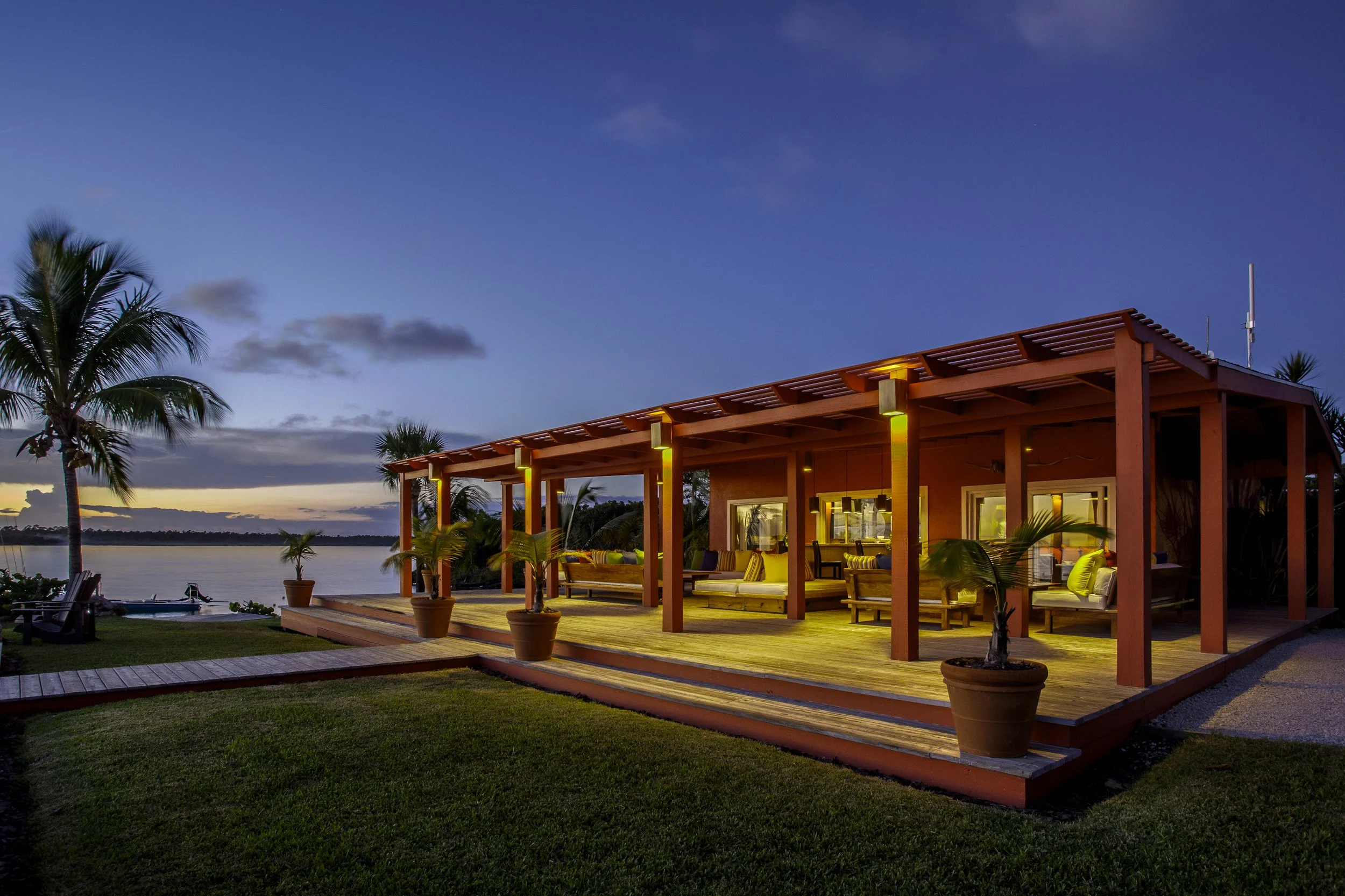 Abaco Lodge in the Bahamas showing an outdoor patio area at dusk with wooden deck, potted plants, and a building with lit windows and seating.