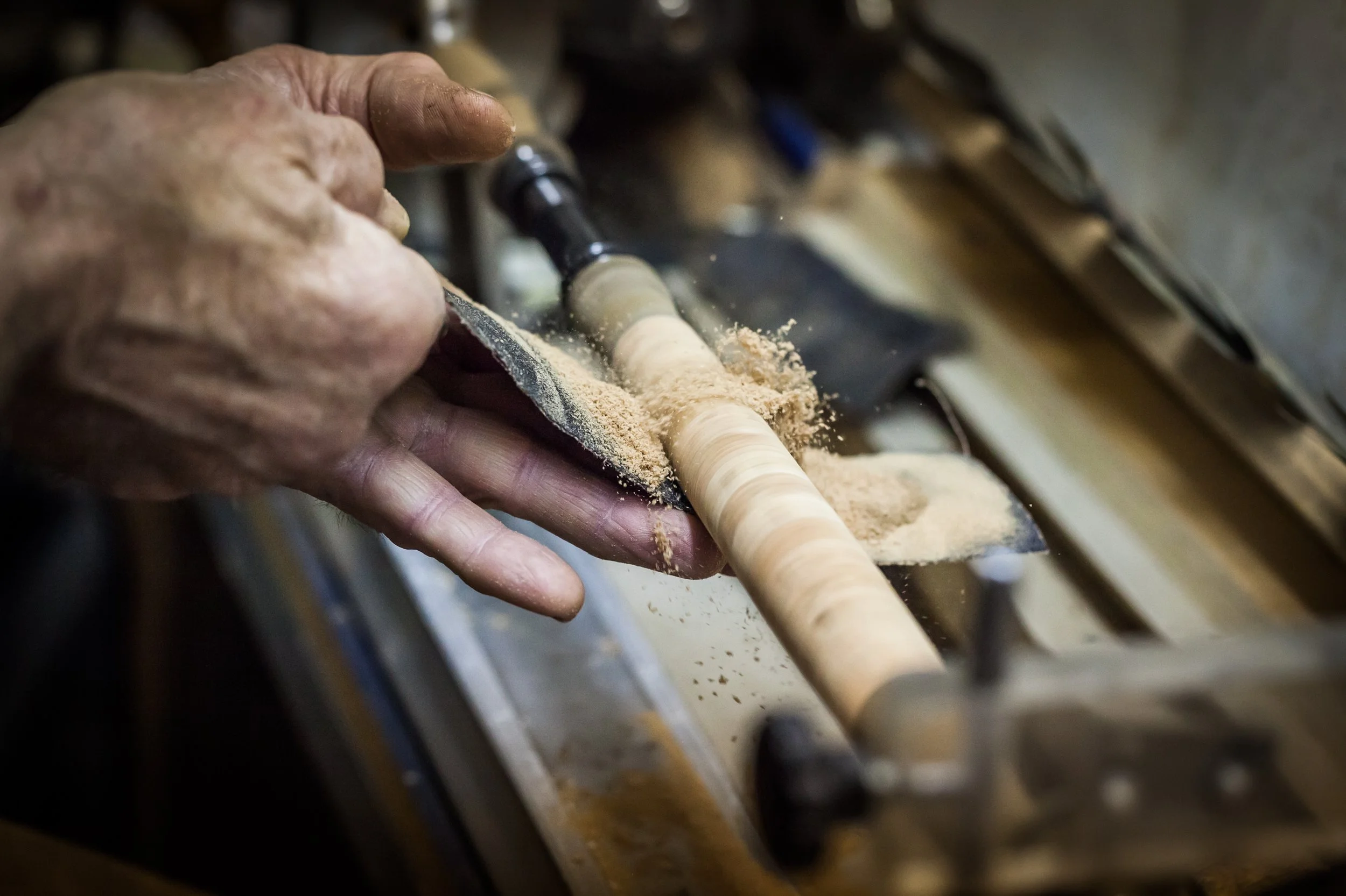 A person operating a woodworking lathe, shaping a piece of wood with wood shavings flying around.